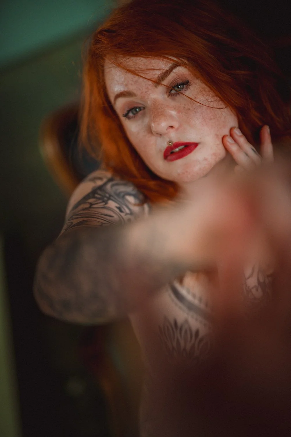 Close-Up einer Frau mit lockigen, roten Haaren im Studio mit Blick in die Kamera mit Tattoos in Witten – von pixelfeder