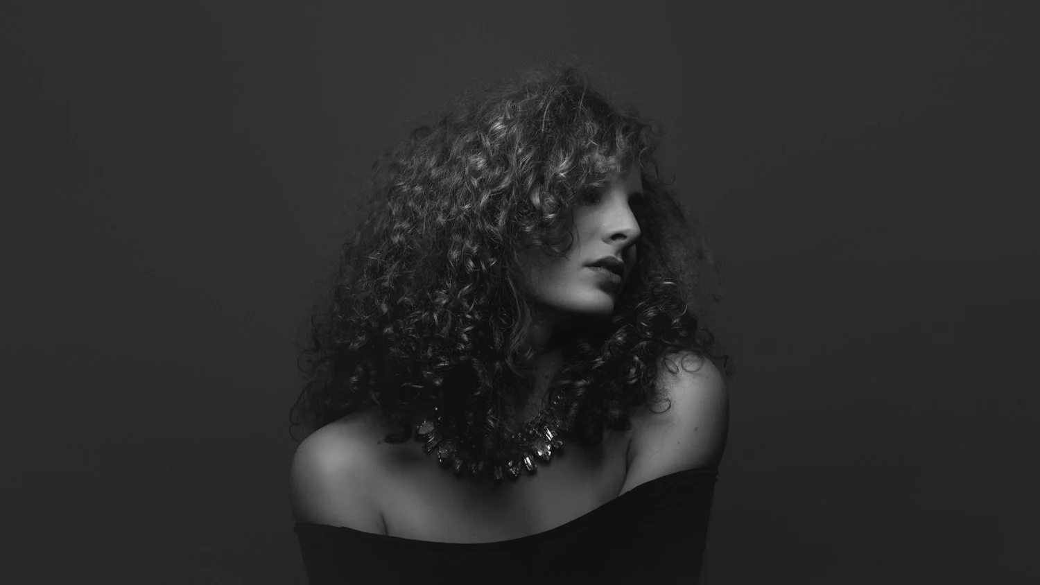 Portrait einer Frau mit lockigen Haaren mit schulterfreiem Oberteil im Studio in Darmstadt – Schwarz-Weiß von pixelfeder