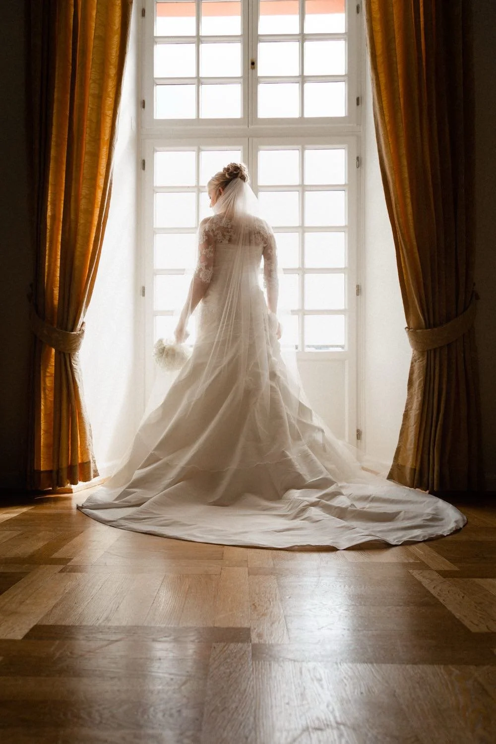 Braut im Hochzeitskleid steht vor einem großen Fenster mit goldenen Vorhängen in Darmstadt – von pixelfeder