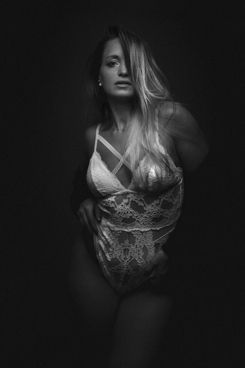 Schwarz-weiß-Fotografie einer Frau in Spitze-Lingerie, die mit einem dunklen Hintergrund posiert.