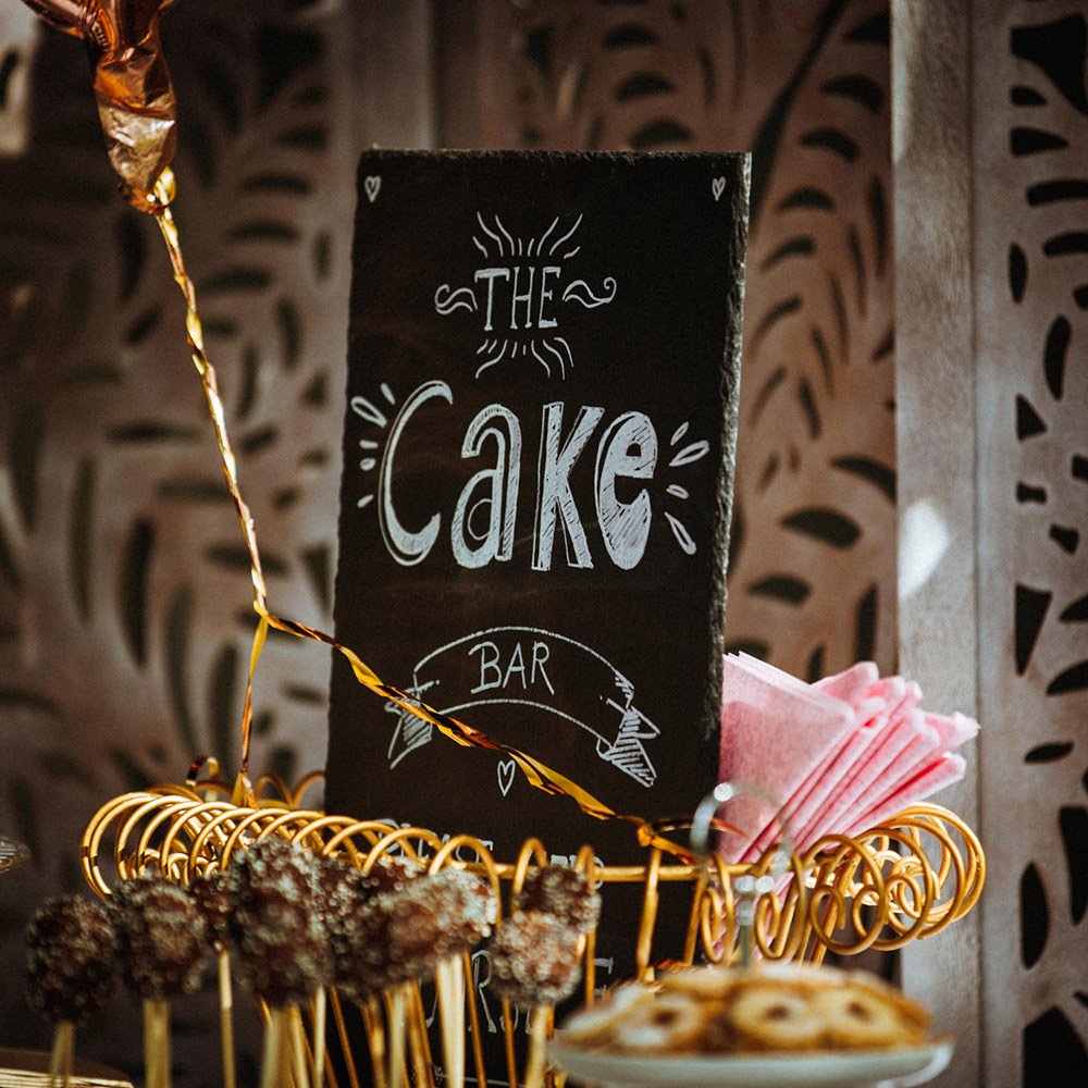 Ein Schwarzes Brett mit der Aufschrift "The Cake Bar" in einer Kuchenecke mit Süßigkeiten und Servietten.