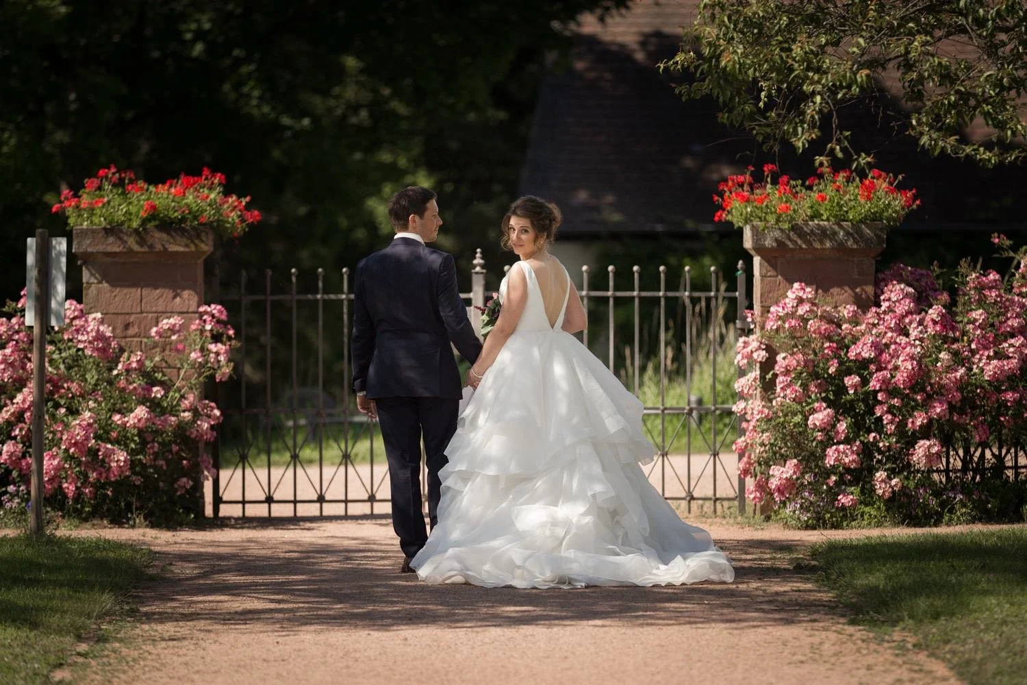 Ein Brautpaar hält Händchen und geht durch ein Tor auf einem Gartenweg in Darmstadt – von pixelfeder