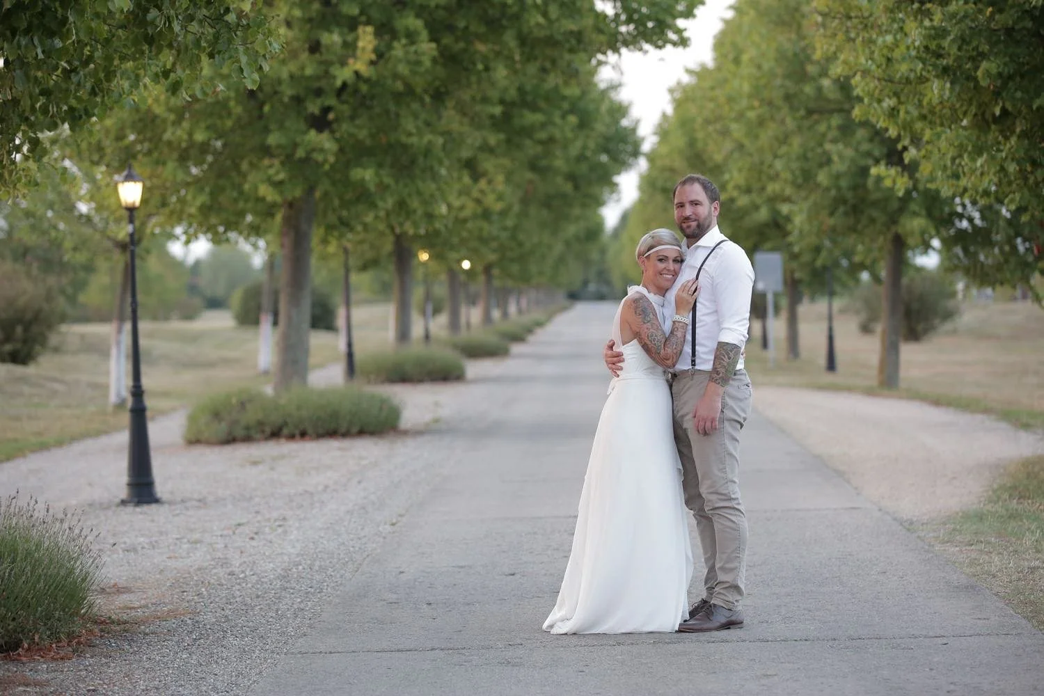 Ein Brautpaar steht auf einem Baumweg, umgeben von grünen Bäumen, bei Sonnenuntergang in Darmstadt – von pixelfeder
