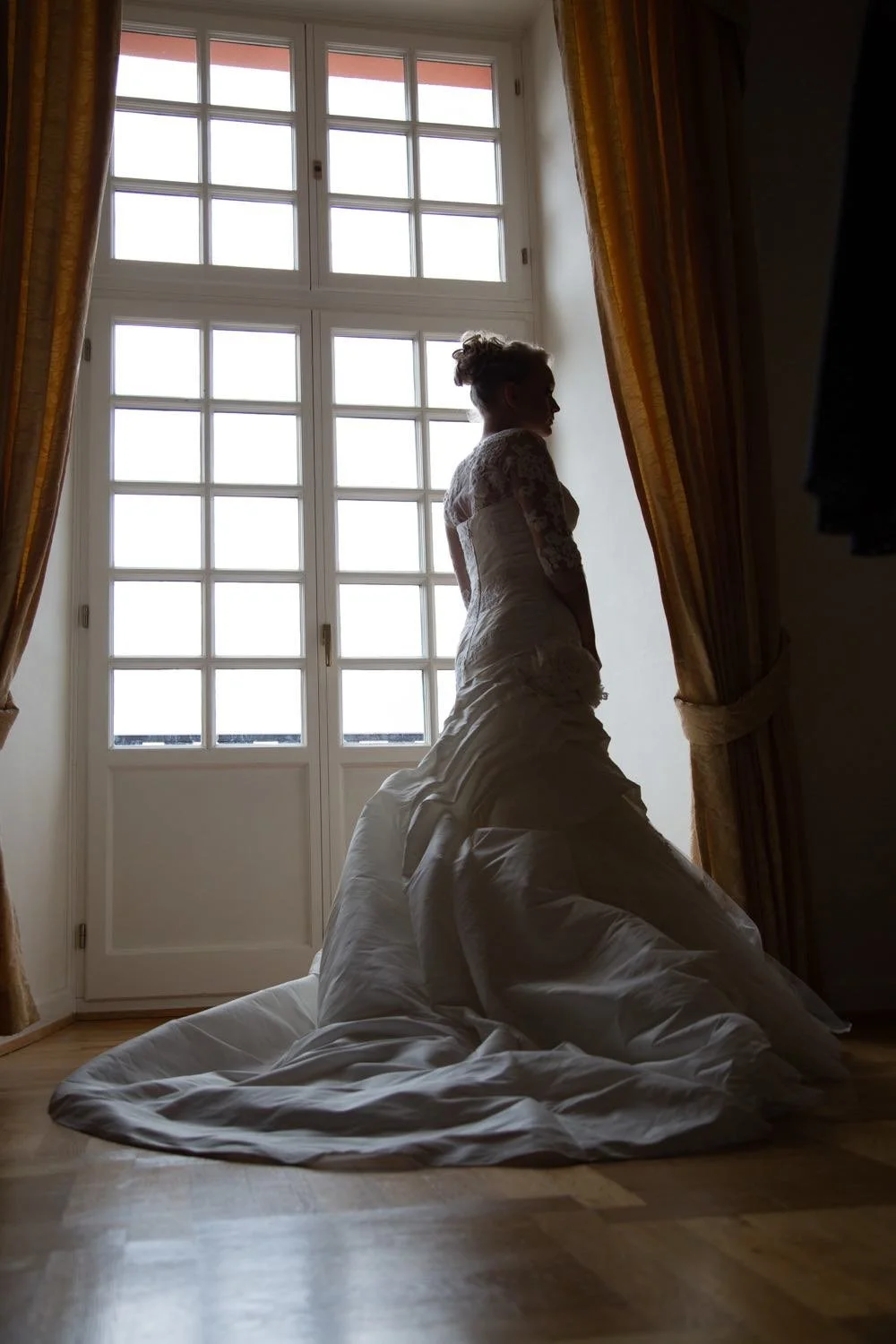 braut im Hochzeitskleid steht vor einem großen Fenster mit goldenen Vorhängen in Darmstadt – von pixelfeder