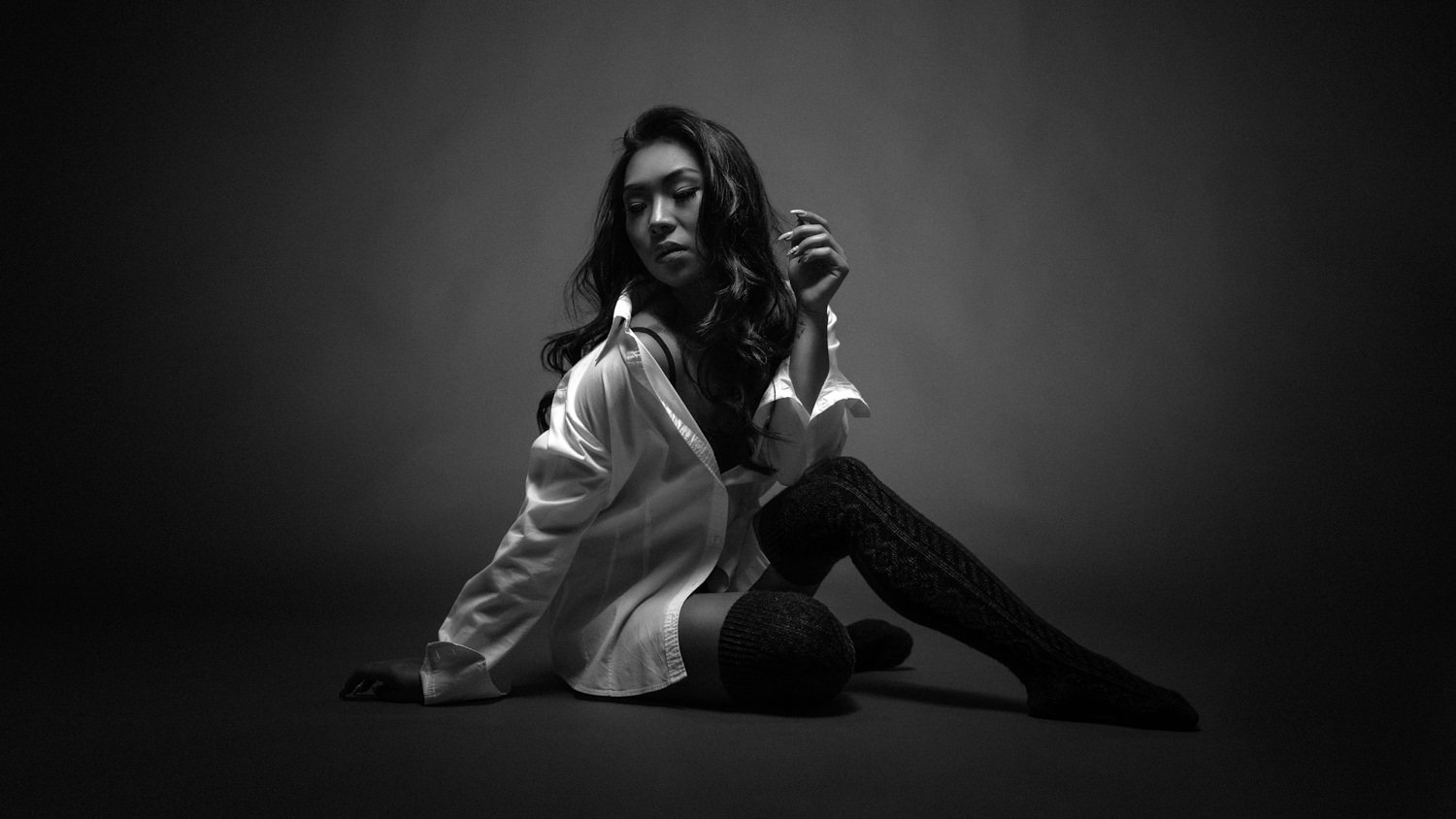 Portrait einer Frau mit offenen, schwarzen Haaren im Studio auf dem Boden sitzend in Darmstadt – Schwarz-Weiß von pixelfeder