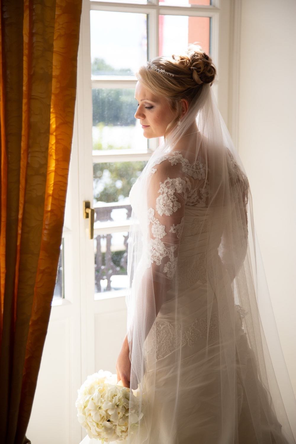 Braut in Hochzeitskleid mit Schleier und Blumenstrauß steht vor Fenster in Darmstadt – von pixelfeder