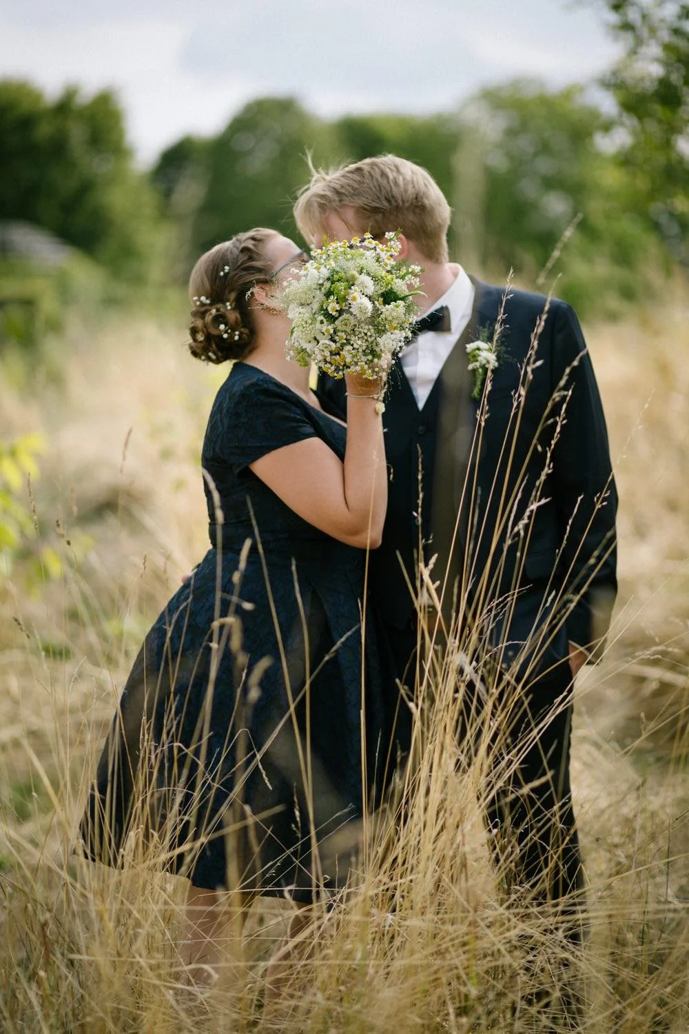 hochzeitspaar beim paarshooting in einem Feld mit hohen Gräsern, sie küsst sich in Darmstadt – von pixelfeder