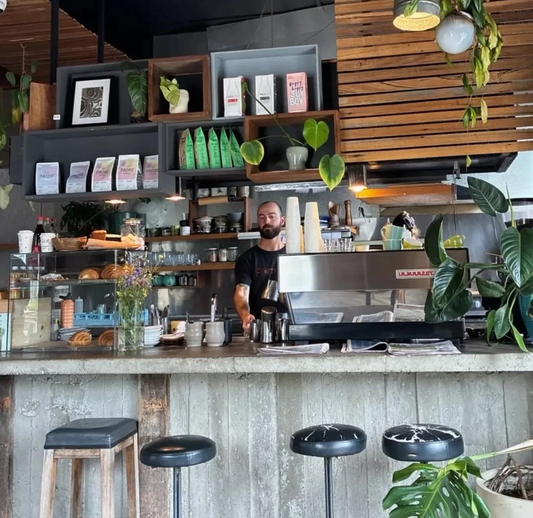 male barista making a coffee at a concrete bench surrounded by plants