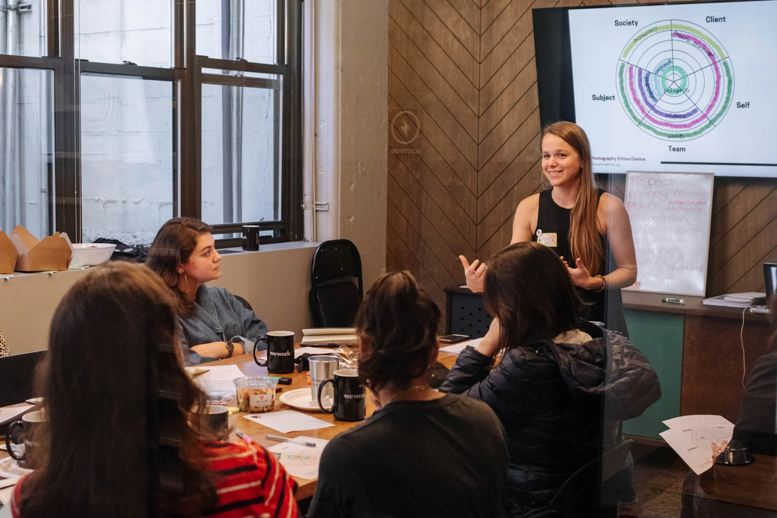 Woman stands at head of table speaking to a group of women seated in a conference room