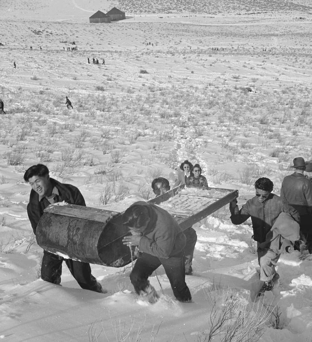 The original caption for this photograph reads: "Tule Lake Relocation Center, Newell, California. A pleasant Sunday afternoon's recreation is spent by evacuee winter sports enthusiasts, on the slopes of Castle Mountain. Homemade sleds and various other homemade pieces of equipment were used by these young people."