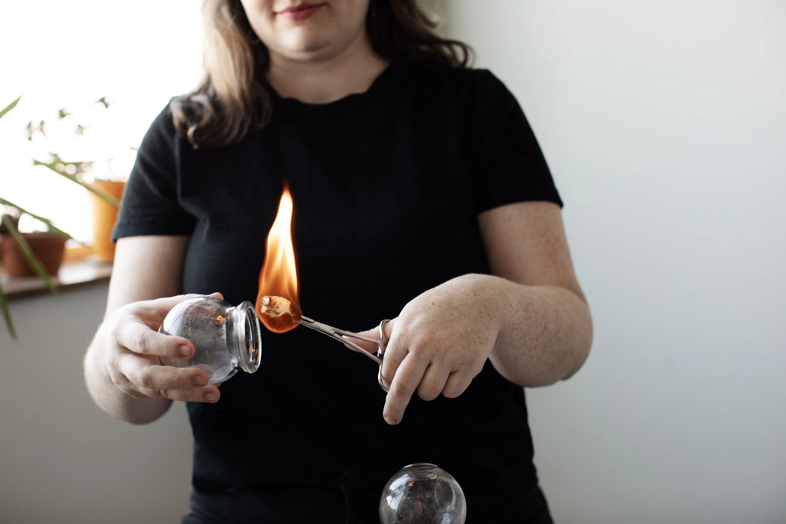 A practitioner with light skin and medium brown hair inserts a flame into a glass cup, preparing to apply it to a patient's back.