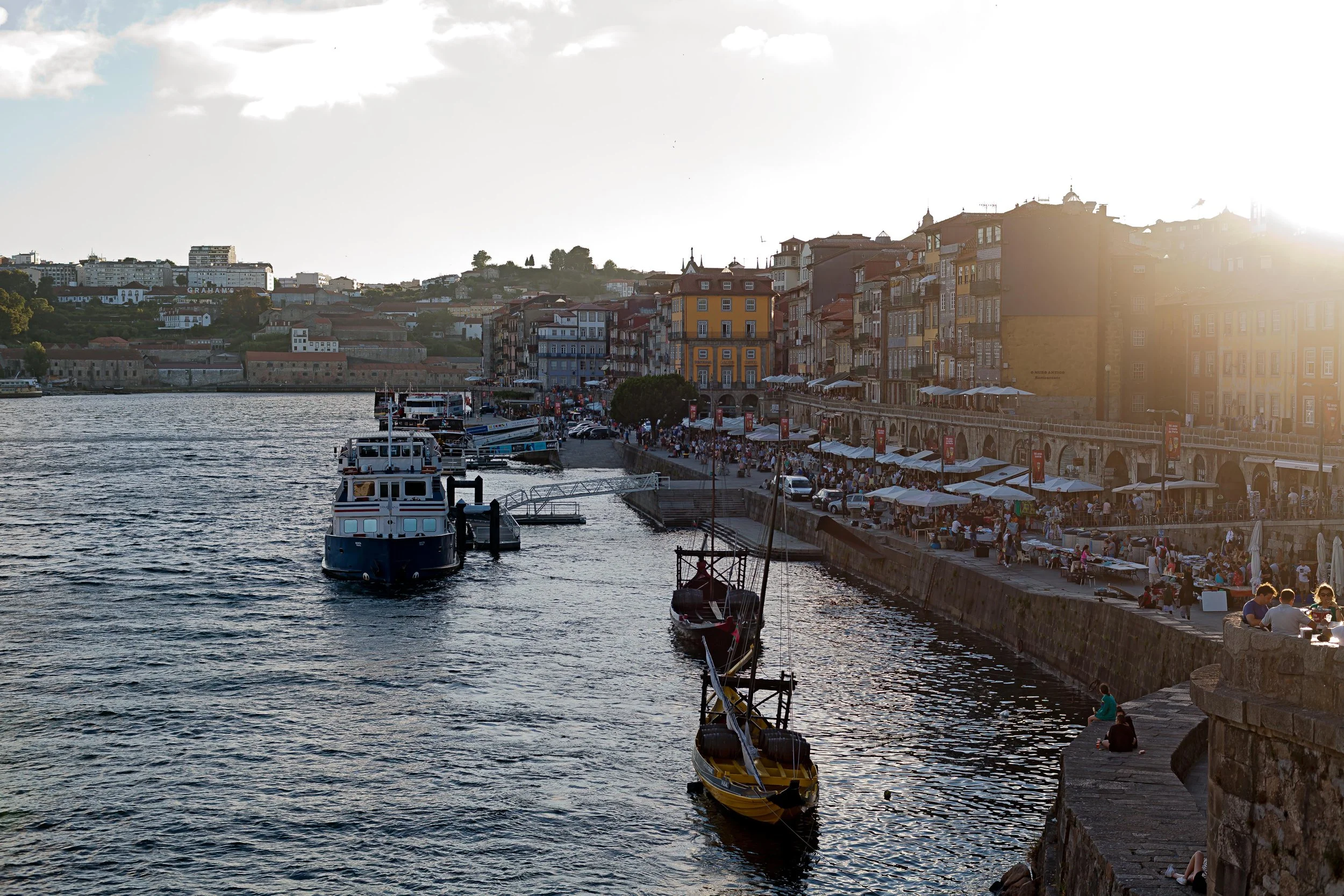 people crowding the space on the river bank, small vessels on the river
