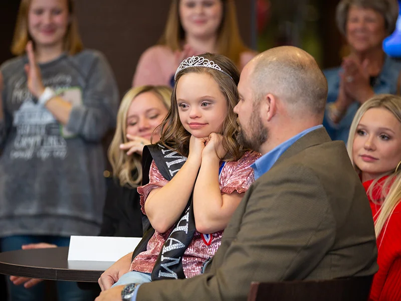 Brad Armstrong holds Aubrey during her Children’s Miracle Network Hospitals Champion celebration while their family and friends observe.
