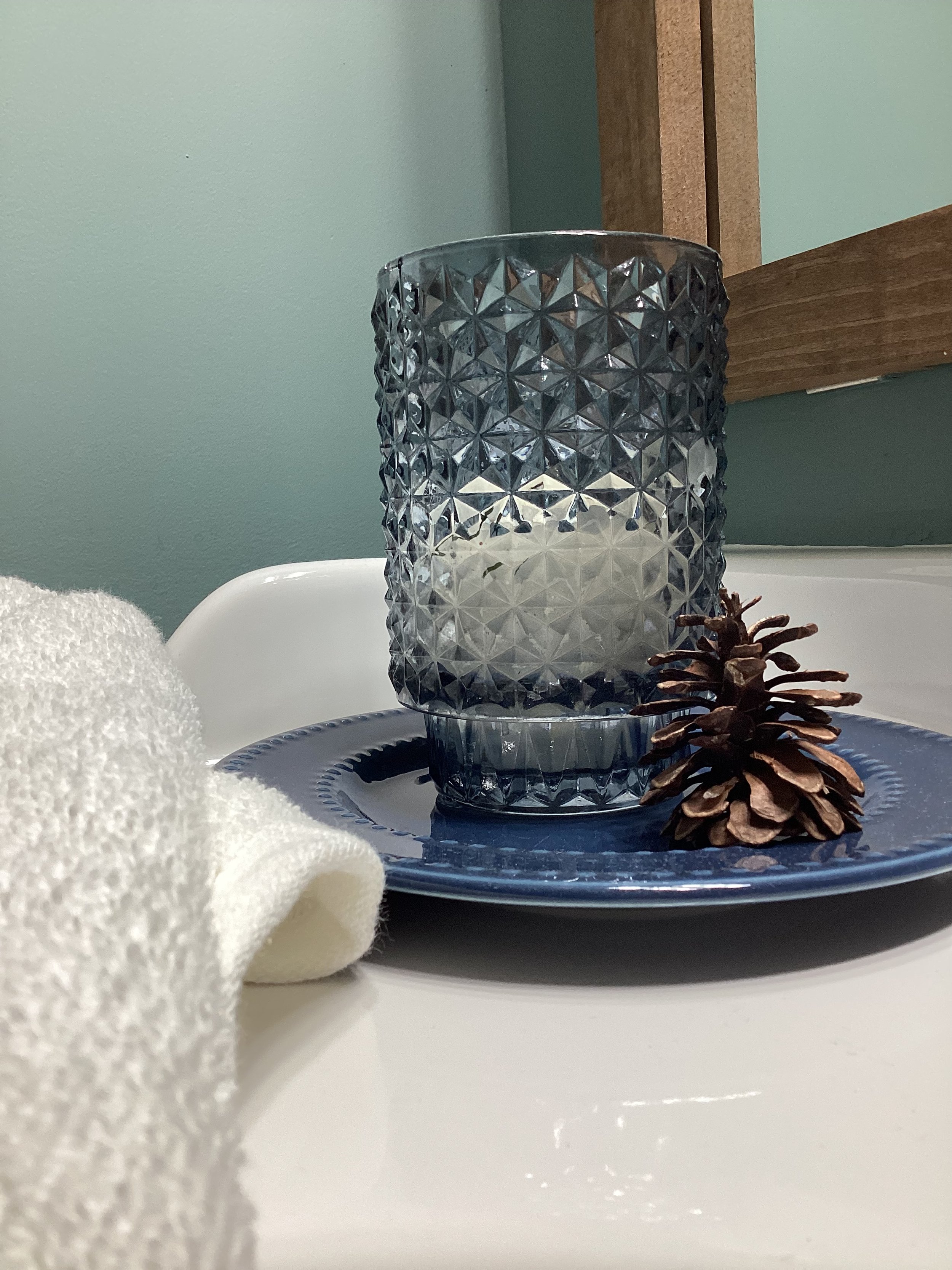 blue dish beside bathroom sink holding blue glass candle and a single pinecone