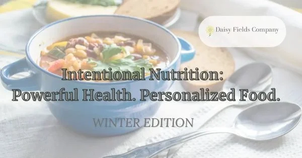 Hearty vegetable soup in a blue ceramic bowl, garnished with herbs and served with whole grain bread—featured in Daisy Fields Company's Winter Edition of Intentional Nutrition.