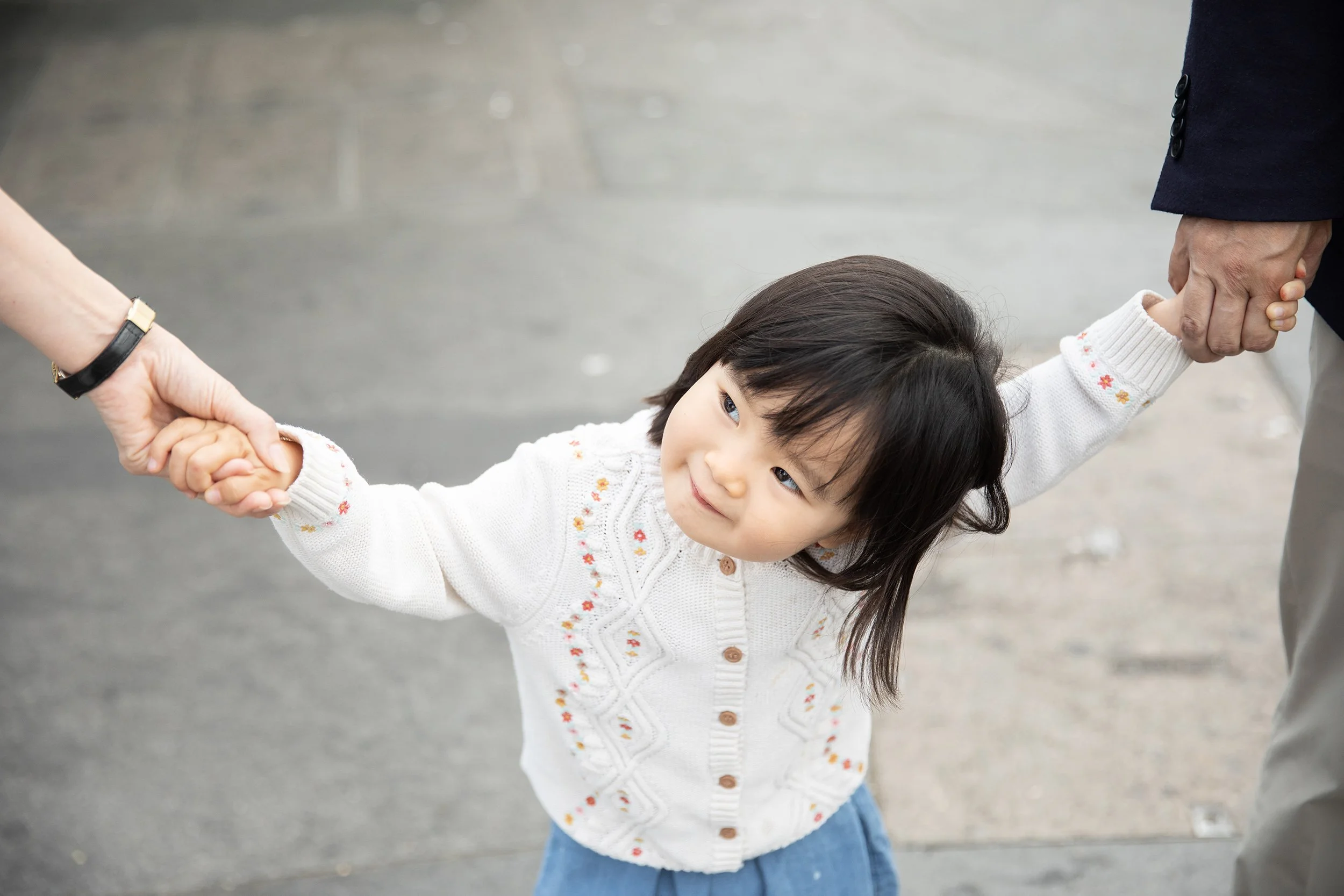 a happy girl holding her parents' hands