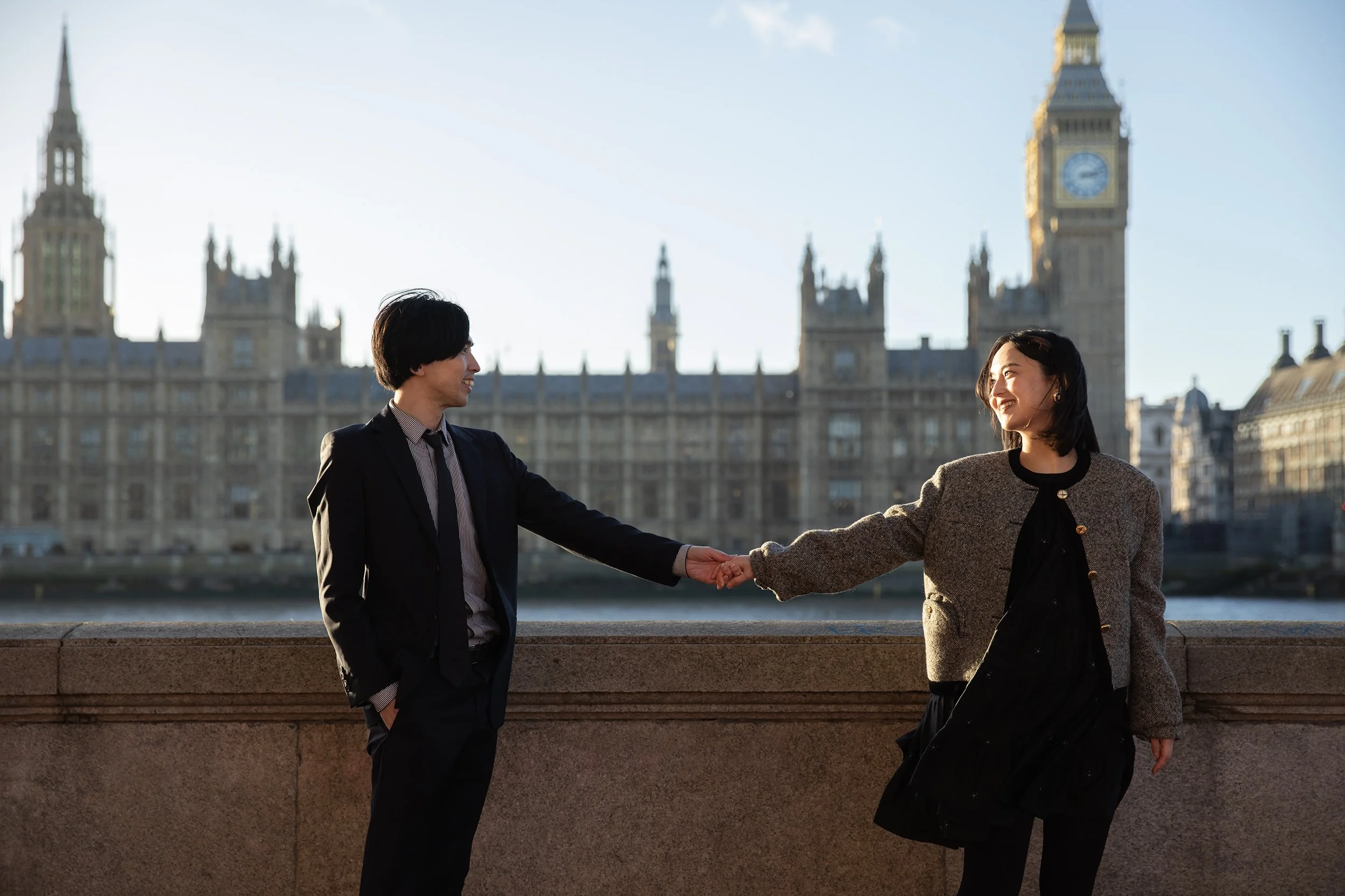 a couple holding hands in front of Houses of Parliament at sunset