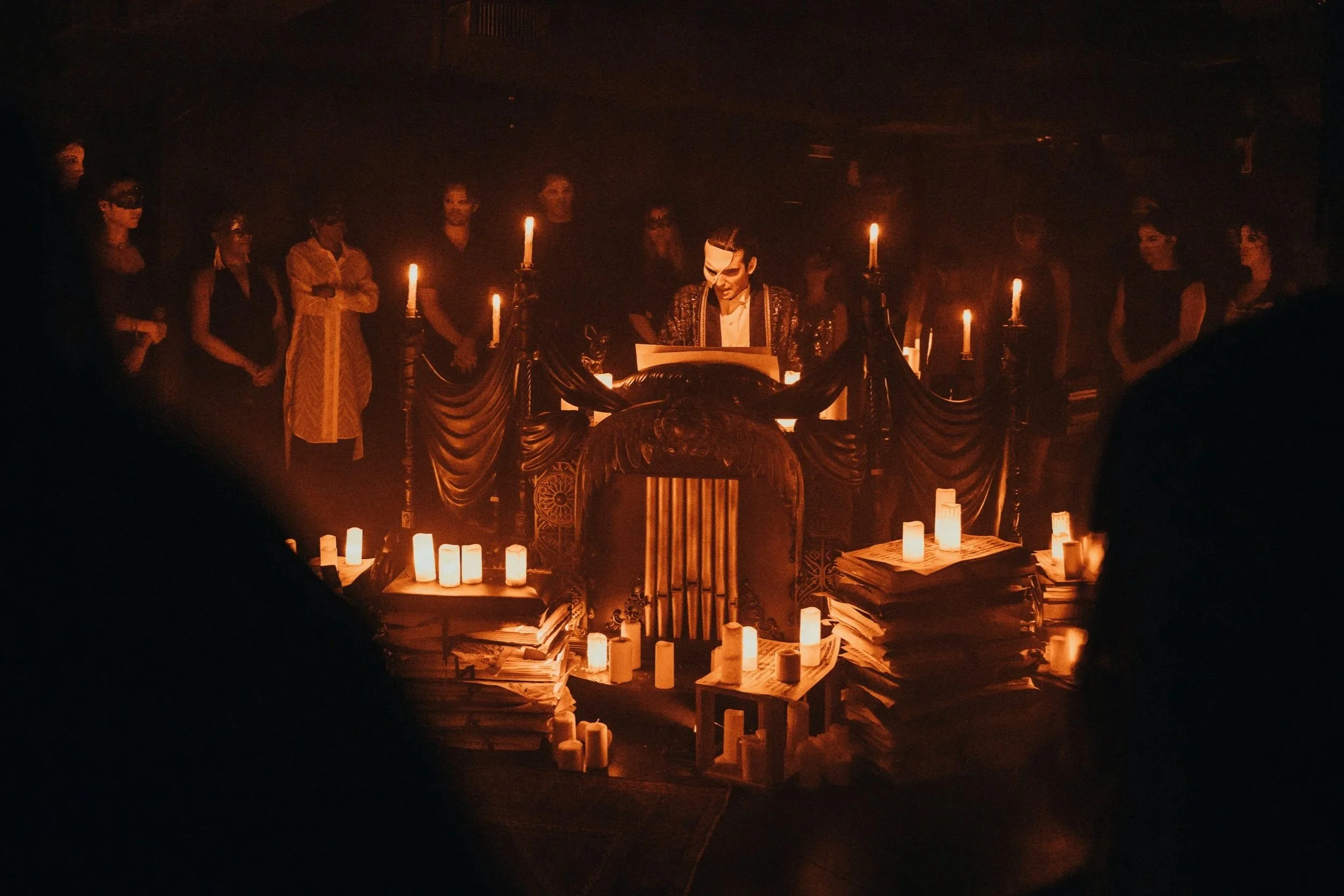 A masked mad stands at a piano, surrounded by candlelight.