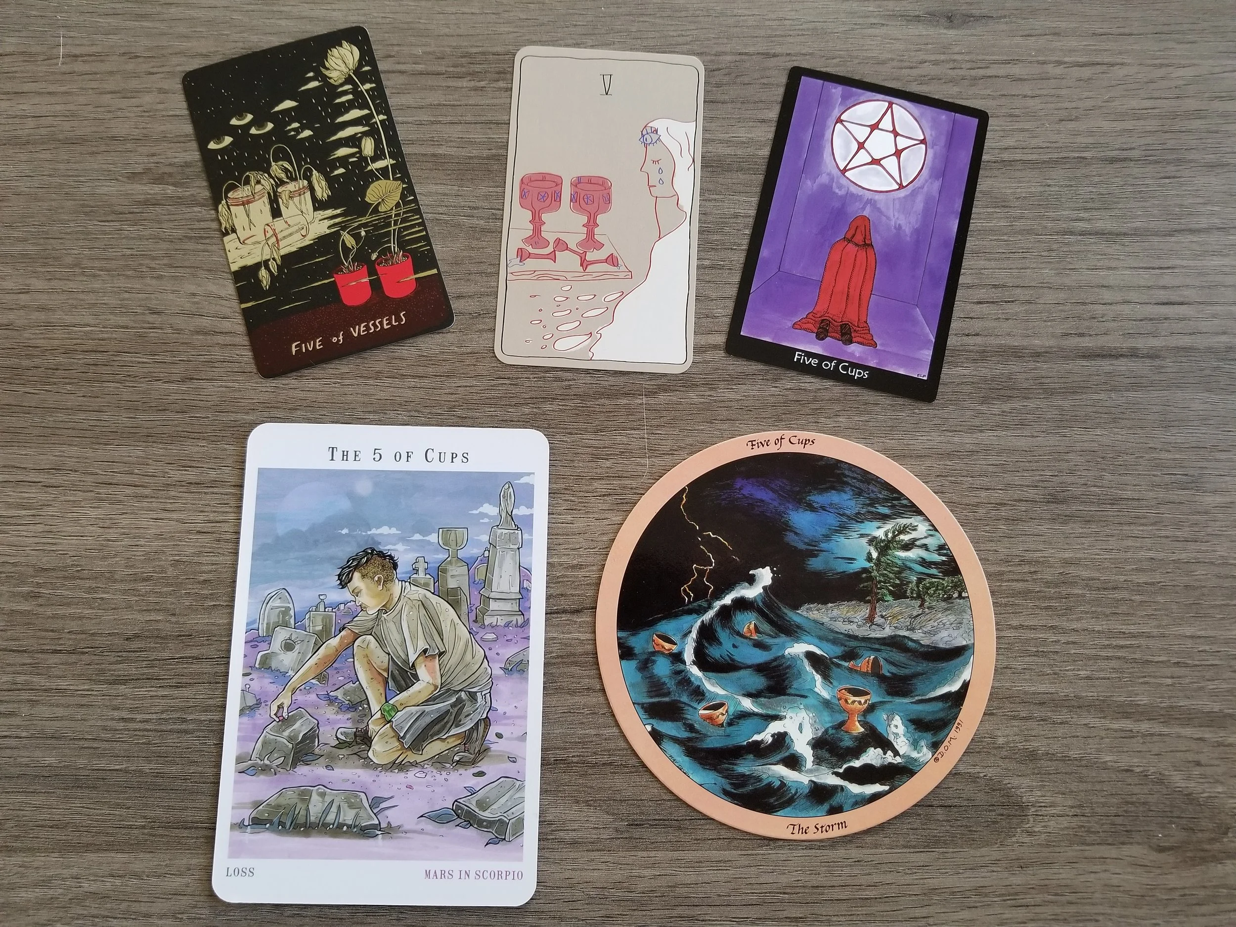 Five of Cups from the Slow Holler Tarot, Personal Space Tarot, Tarot of the Crone, Next World Tarot, and the Daughters of the Moon Tarot