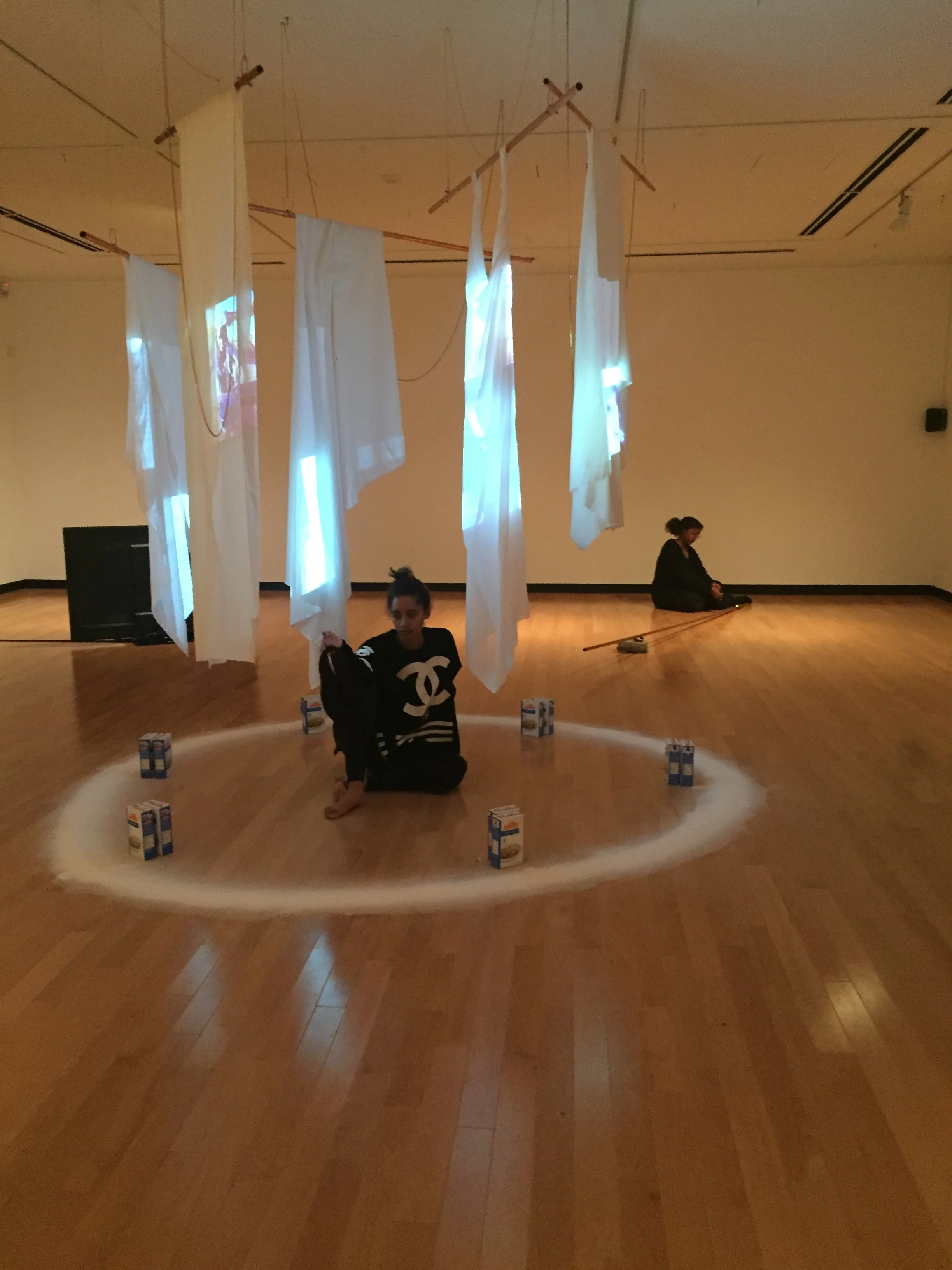 Jessica Karuhanga and Maandeeq Mohamed in through a brass channel. Jessica sits within- future ghosts - 2017, Single-channel video, Cooper pipe, Cloth, Paper