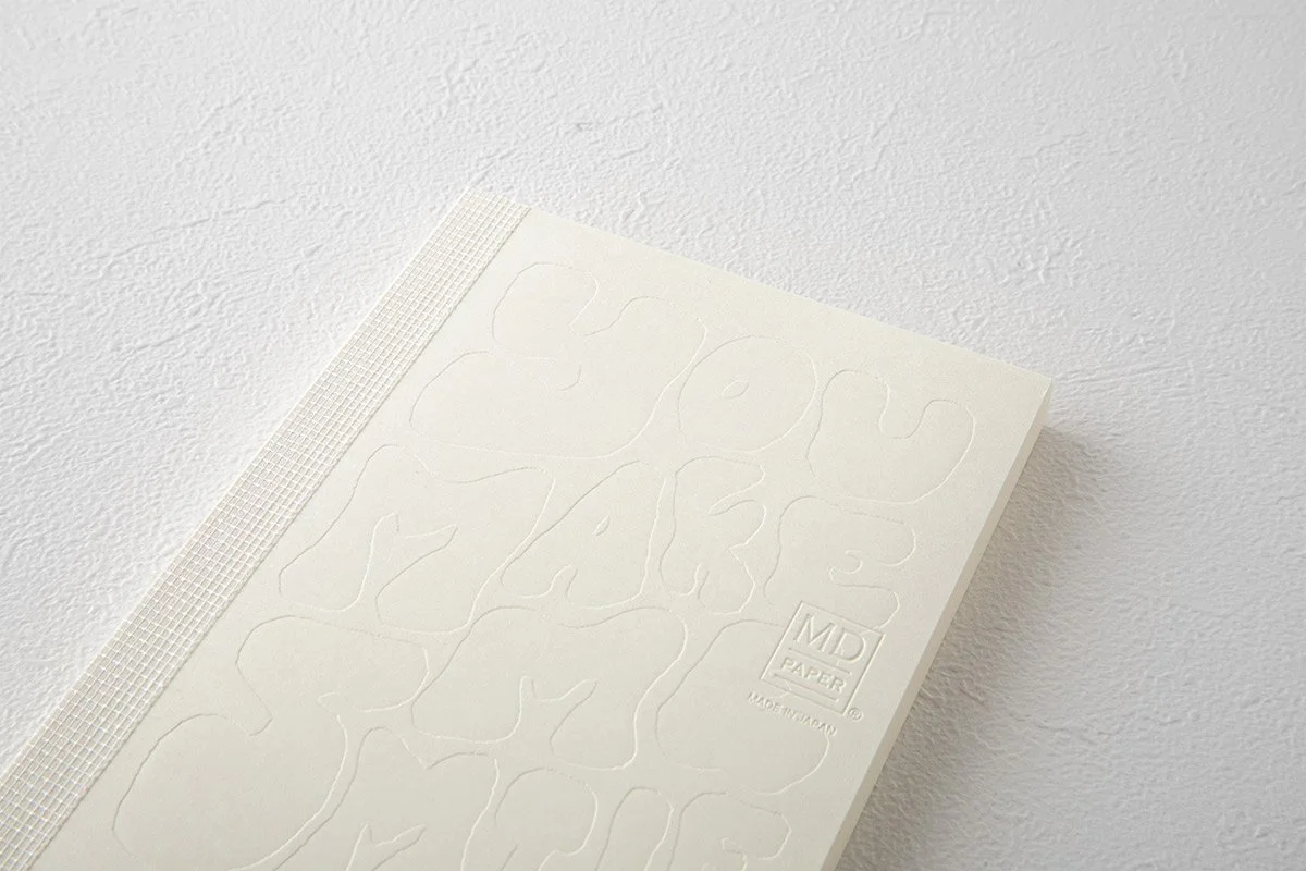 日本を代表する文具メーカーMIDORIが出しているMDノートの15周年を記念して、国内外で活躍する15名のアーティストたちによる周年記念ノートが発売になりました。弊社ではその中の11名をキュレーションさせていただきました。アーティストが『MDノート』の表紙に描いたイラストや文字を、空押しで再現した特別なノートとなっています。                                     We teamed up with authentic stationary brand calle