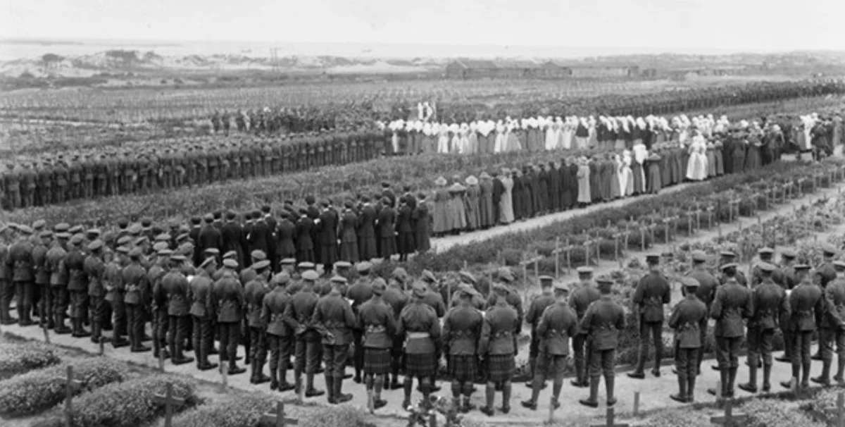Photograph taken by Henry Armytage Sanders recording the memorial service held at the Étaples Military Cemetery on 4 August 1918 commemorating the fourth anniversary of the start of the First World War. Many of those attending – civilians, nurses and military personnel – stand amongst the recently dug war graves.