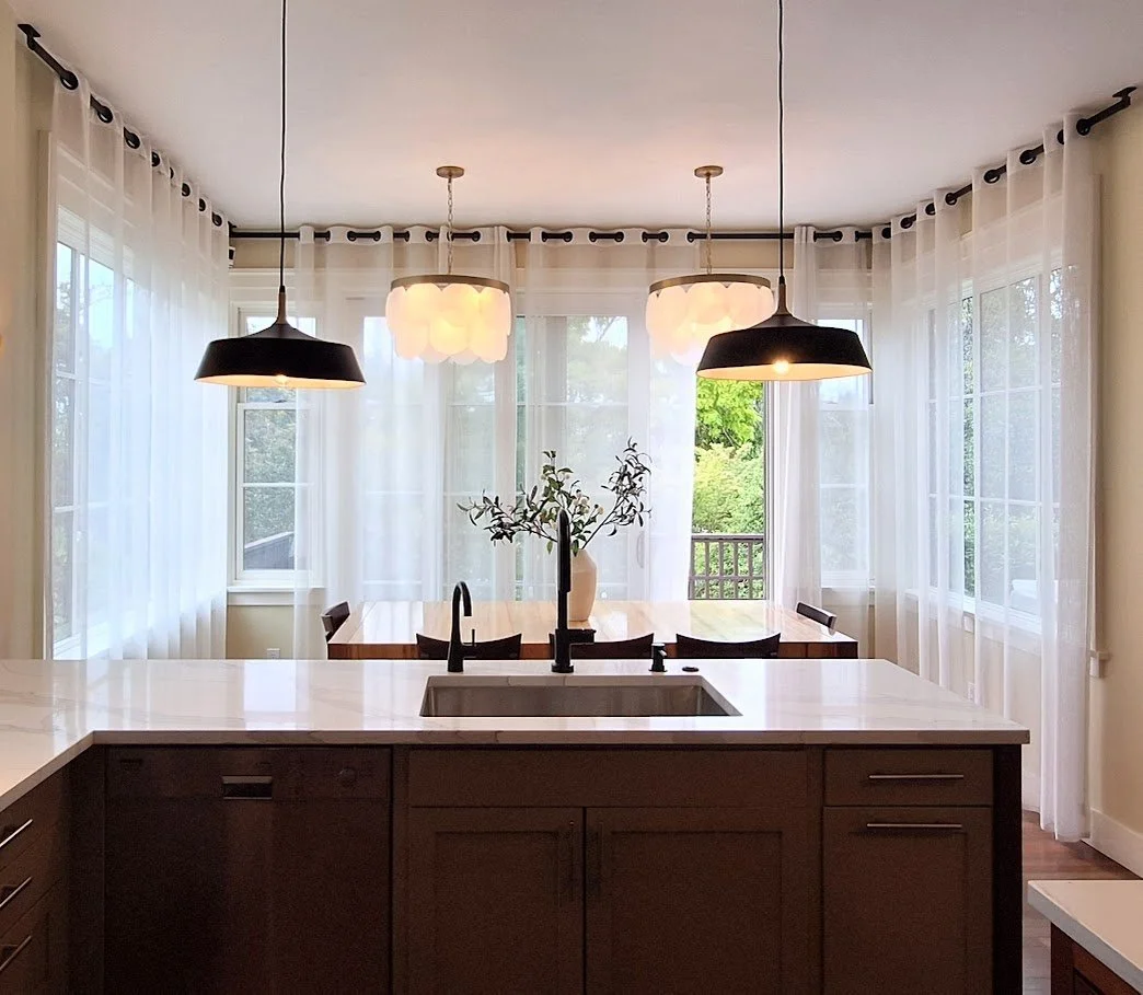 Modern kitchen with midcentury pendants, geosphere chandelier, Calacatta Solessio quartz, dining table, and large windows with sheer curtains.