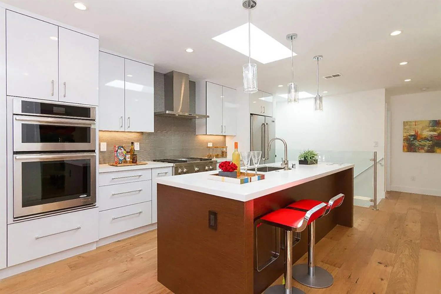 Contemporary kitchen with glossy frameless cabinets, glass tiles backsplash, stainless steel appliances, walnut island with Arctic White quartz, and Bottega Piston bar stools.