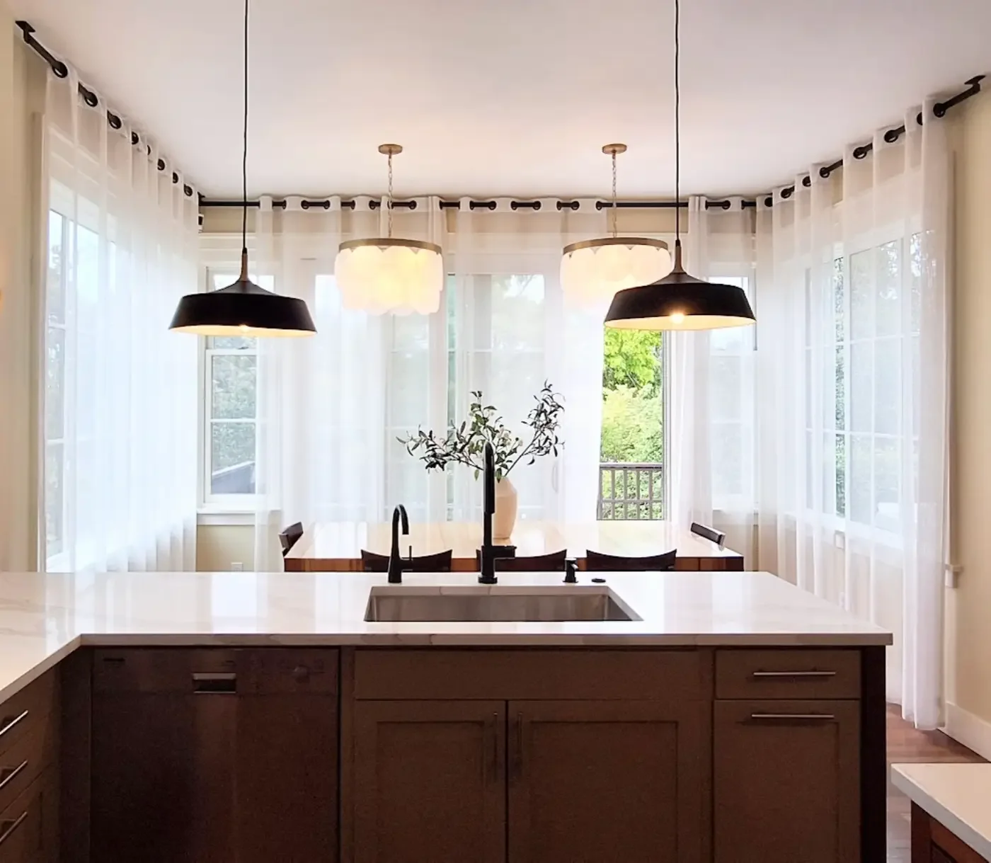 Modern kitchen with midcentury pendants, geosphere chandelier, Calacatta Solessio quartz, dining table, and large windows with sheer curtains.