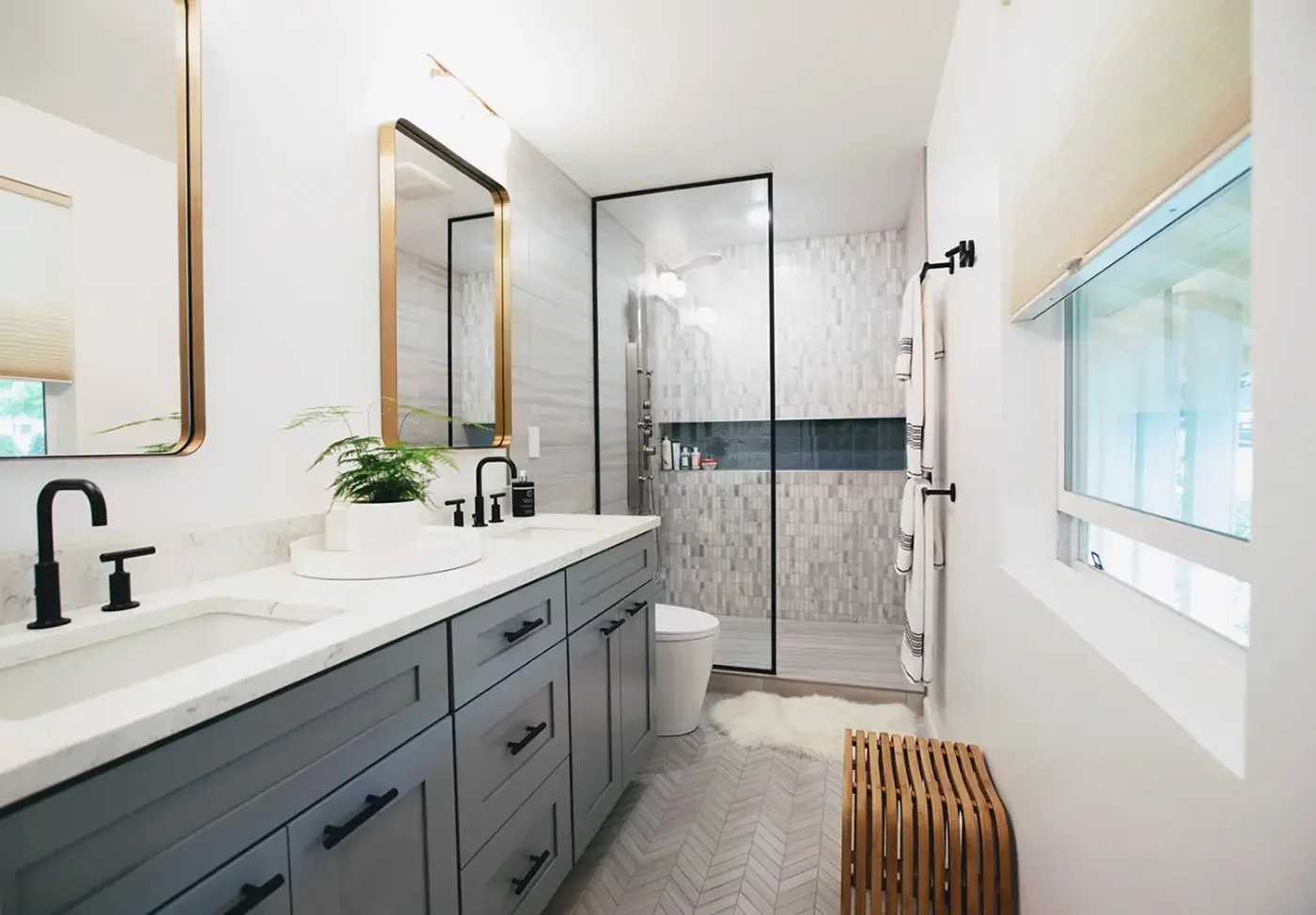 Modern bathroom with double vanity, Calacatta Verona quartz, black fixtures, blue shaker cabinets, gold mirrors, Hunter Douglas blinds, and walk‑in rain shower with marble tile and herringbone porcelain floor.
