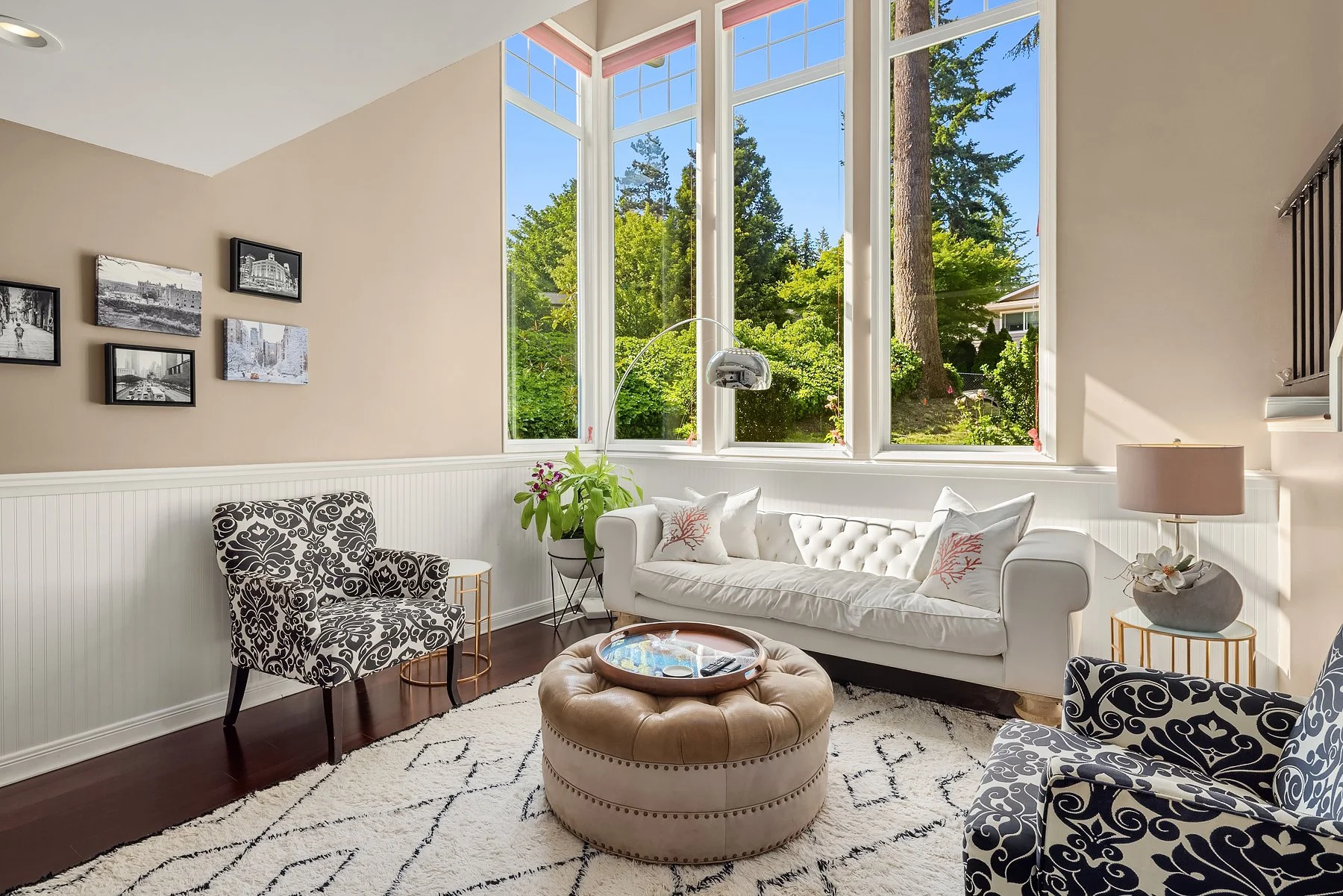 Living room with large picture windows, Noir tufted sofa, damask armchairs, Baker ottoman, and arco lamp—luxury interior design.