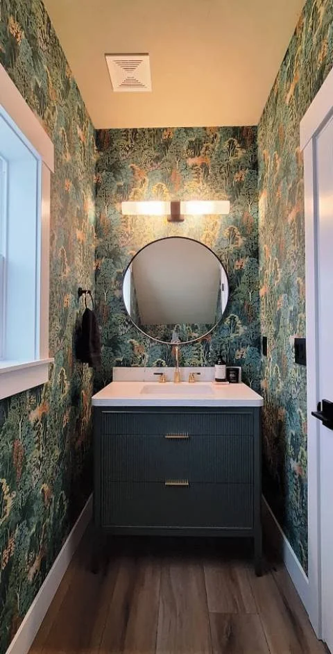 Powder room with Graham & Brown New Eden Emerald wallpaper, fluted marble vanity, black and gold fixtures, round mirror, and LVP flooring.