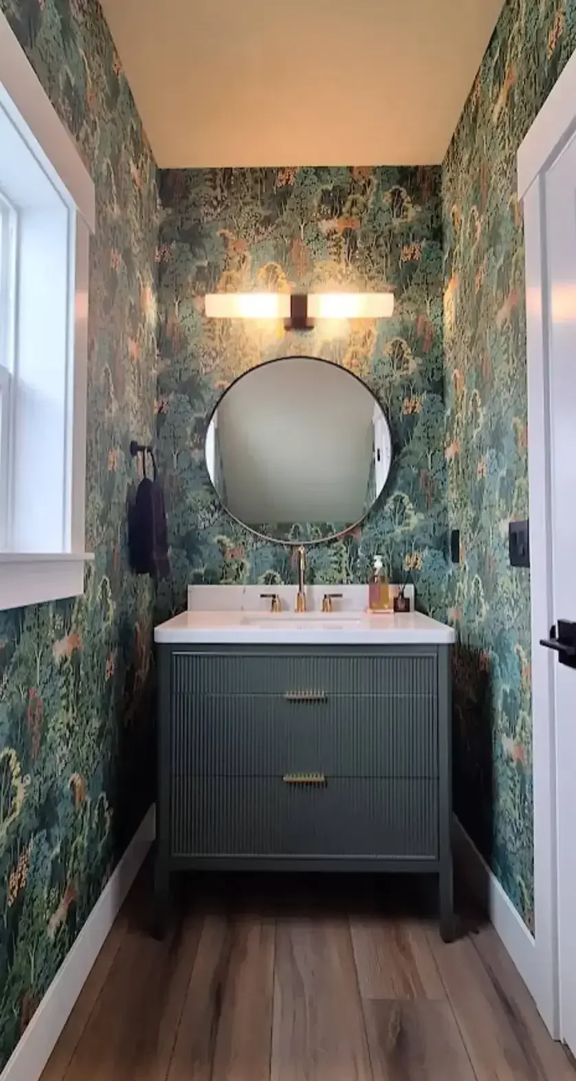 Powder room with Graham & Brown New Eden Emerald wallpaper, fluted marble vanity, black and gold fixtures, round mirror, and LVP flooring.