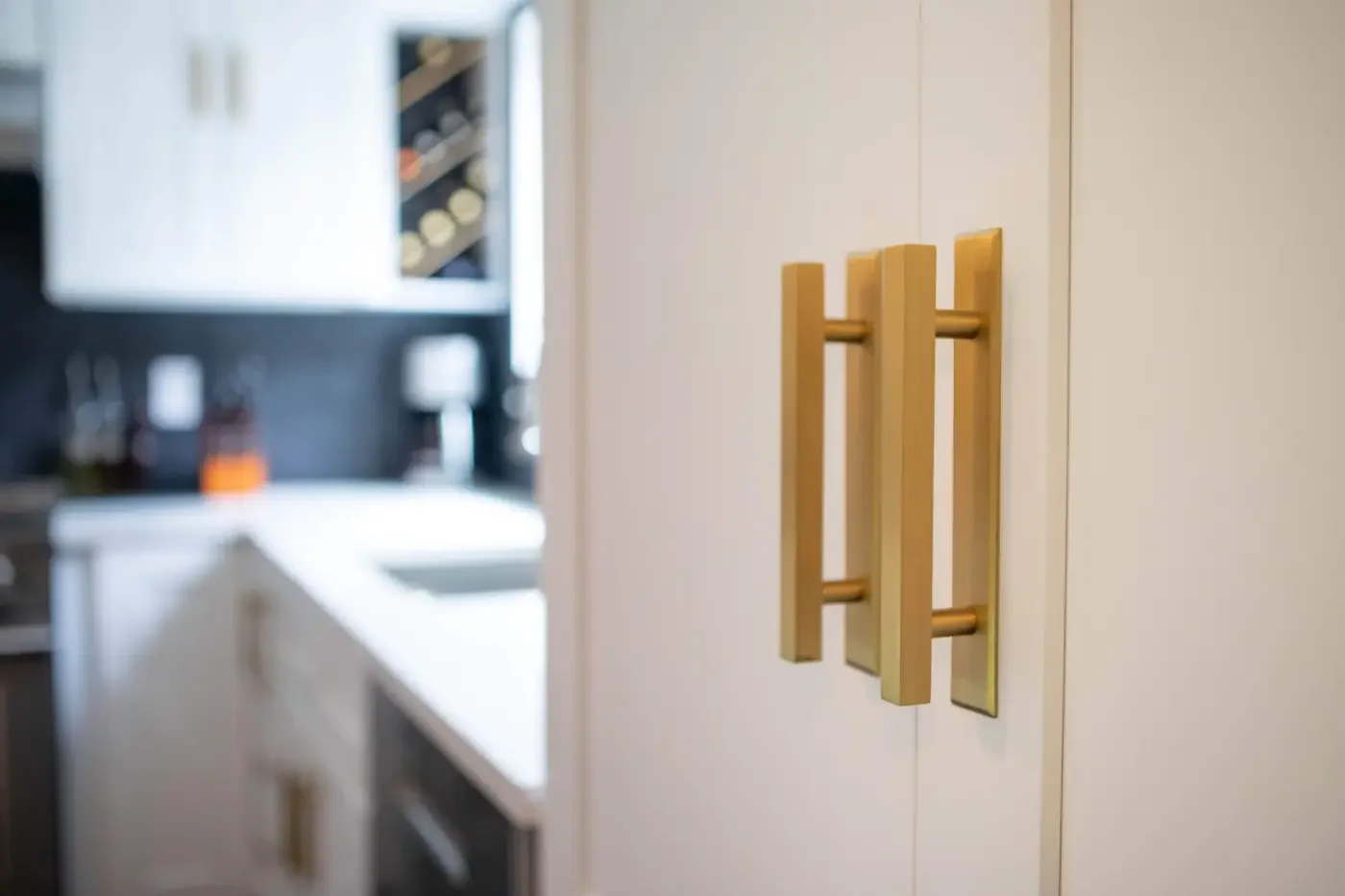 gold hardware and custom wine rack in modern kitchen with white shaker cabinets, Calacatta Laza quartz, and Bedrosians tile backsplash.