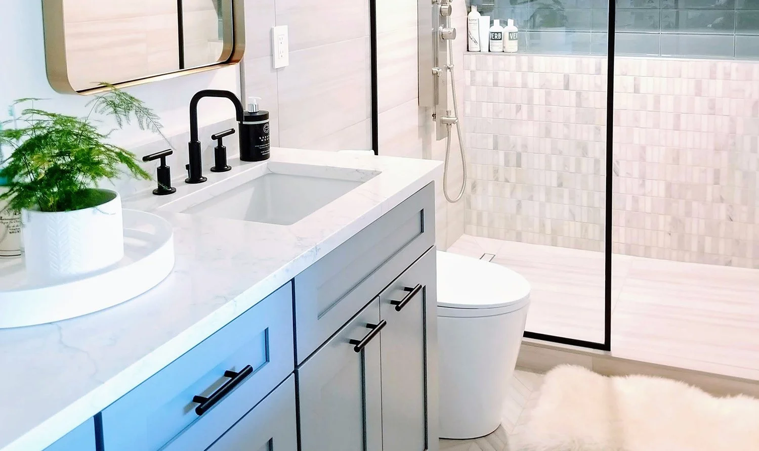 Modern bathroom with double vanity, Calacatta Verona quartz, black fixtures, blue shaker cabinets, gold mirrors, and walk‑in rain shower with marble tile and herringbone porcelain floor.