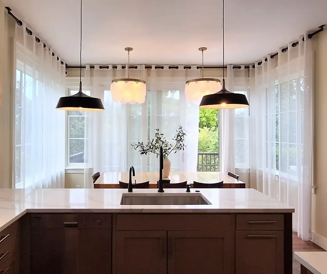 Modern kitchen with midcentury pendants, geosphere chandelier, Calacatta Solessio quartz, dining table, and large windows with sheer curtains.