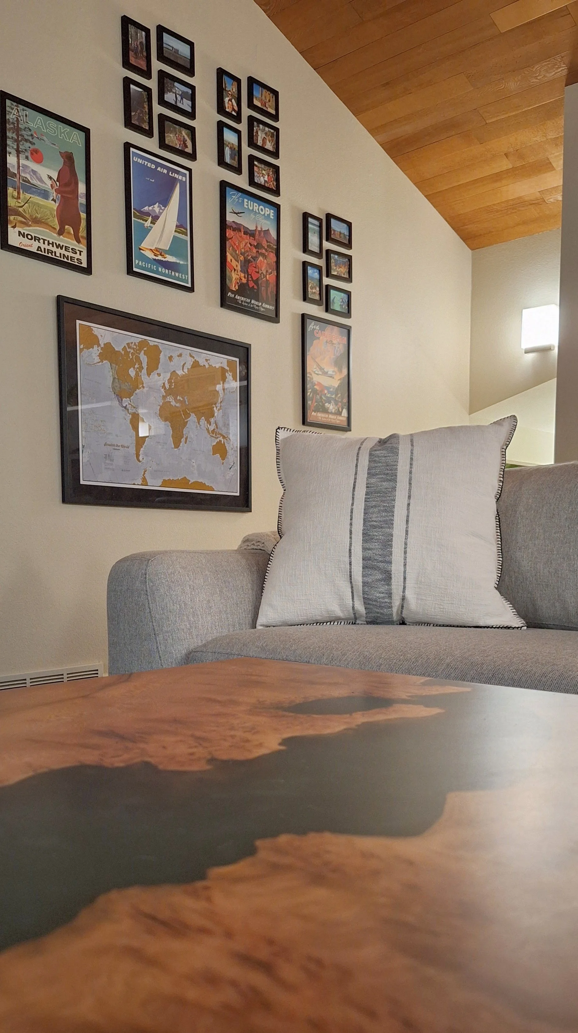 Living room with framed travel collage, Four Hands sofa, Crate & Barrel pillow, wood plank ceiling, and custom sycamore epoxy coffee table.