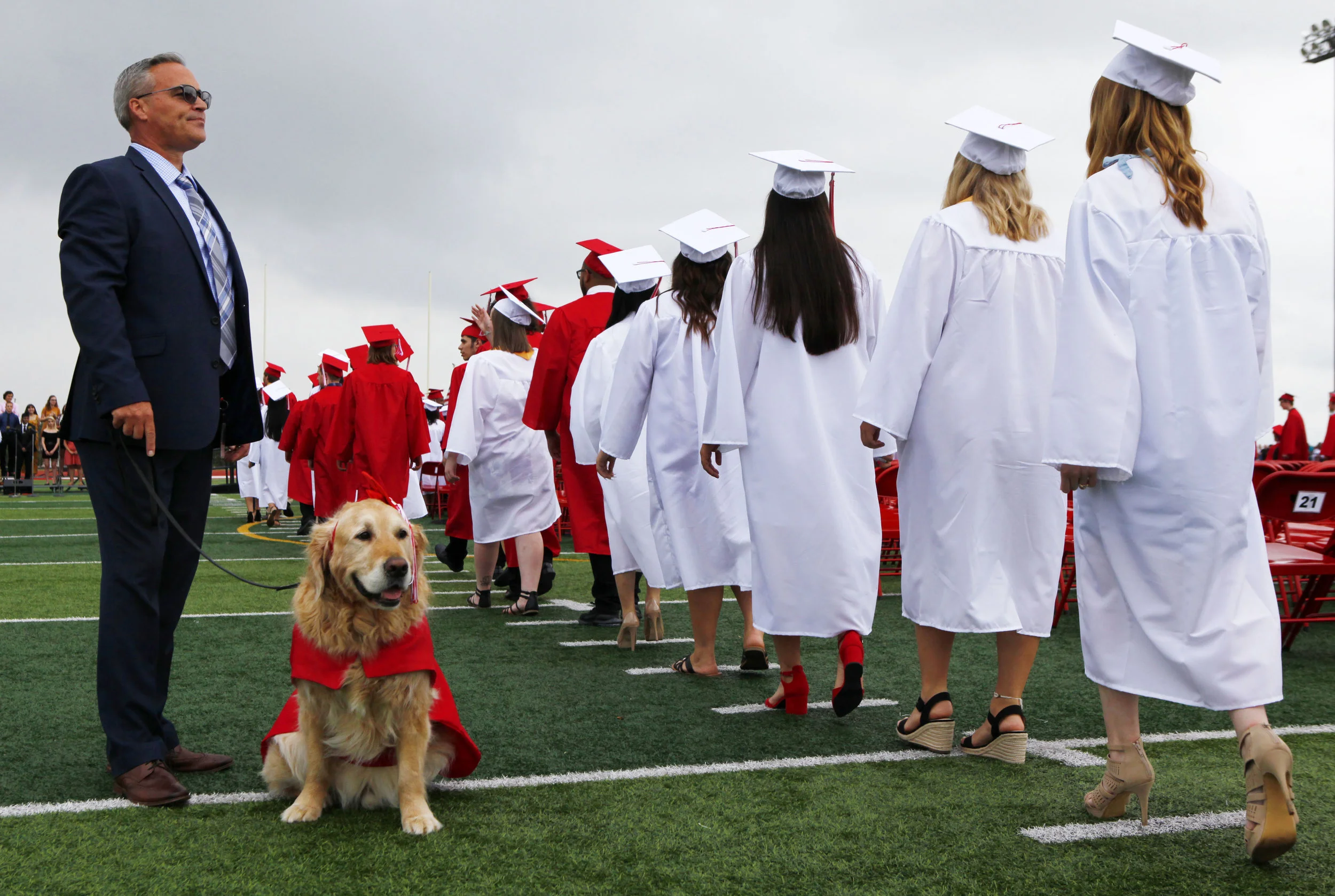 Portage High School dean of students Tim Kunstek, left, and comfort dog Isaiah, watch as graduates proceed onto the football field during commencement.