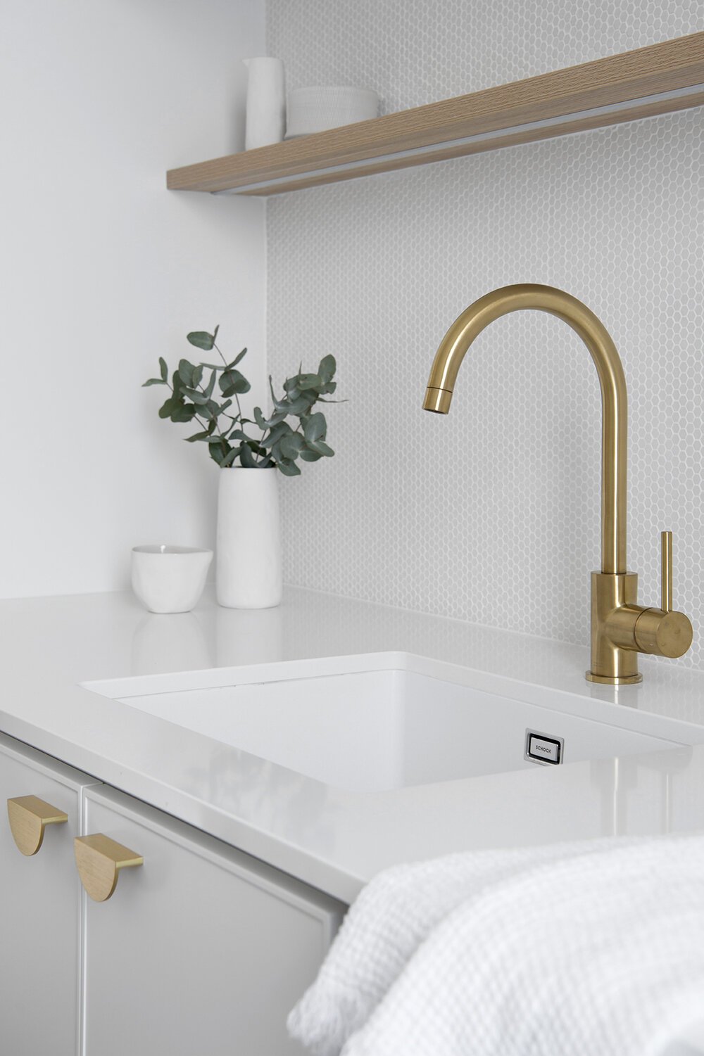 Brass laundry sink faucet with white plant pot in the background in Classic Coastal Laundry Plan laundry room remodel