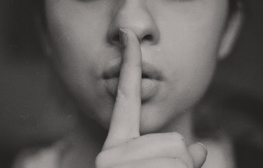 Black and white image of a woman holding her index finger in front of her lips in the "shush" gesture