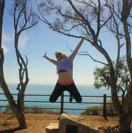 Brooke Houser leaping ecstatically into the air. Behind her is the ocean.