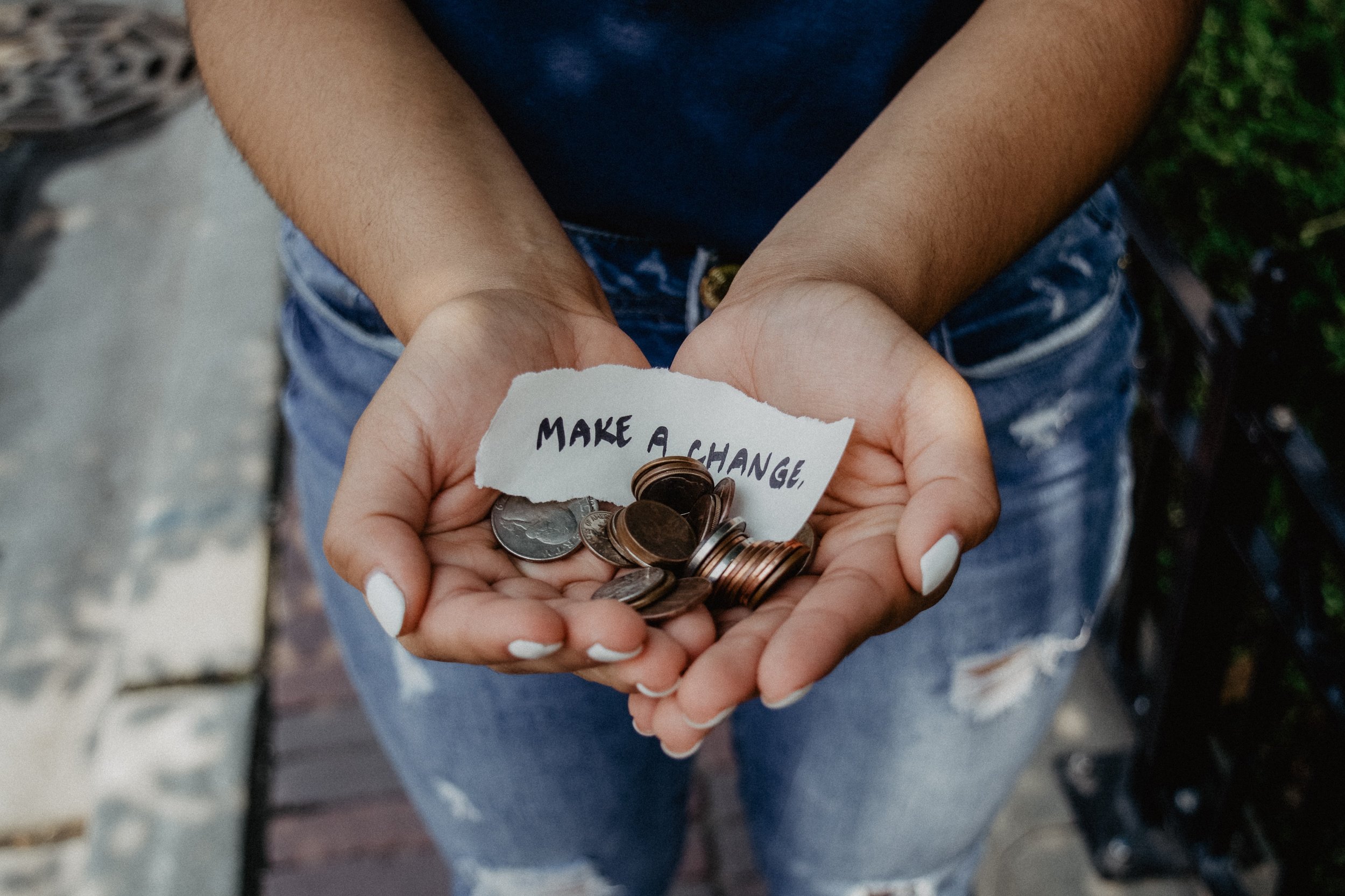 A woman holds coins in her cupped hands, with a slip of paper that reads, "Make a change"