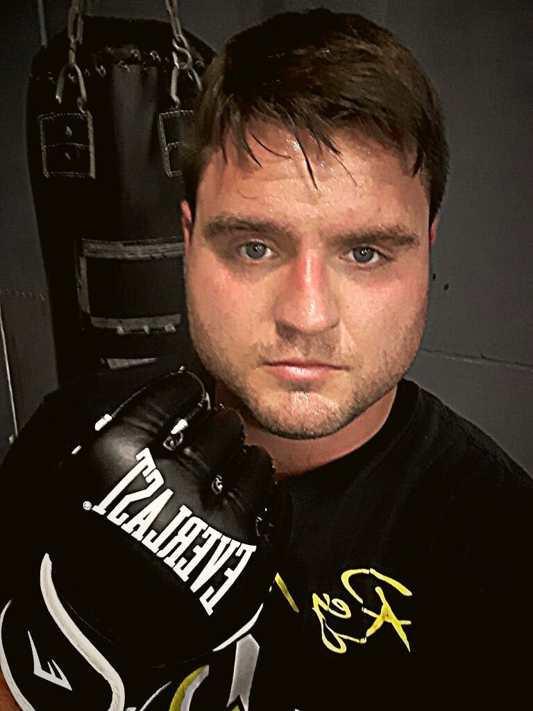 Justin Gillespie wearing boxing gloves, standing in front of a heavy bag