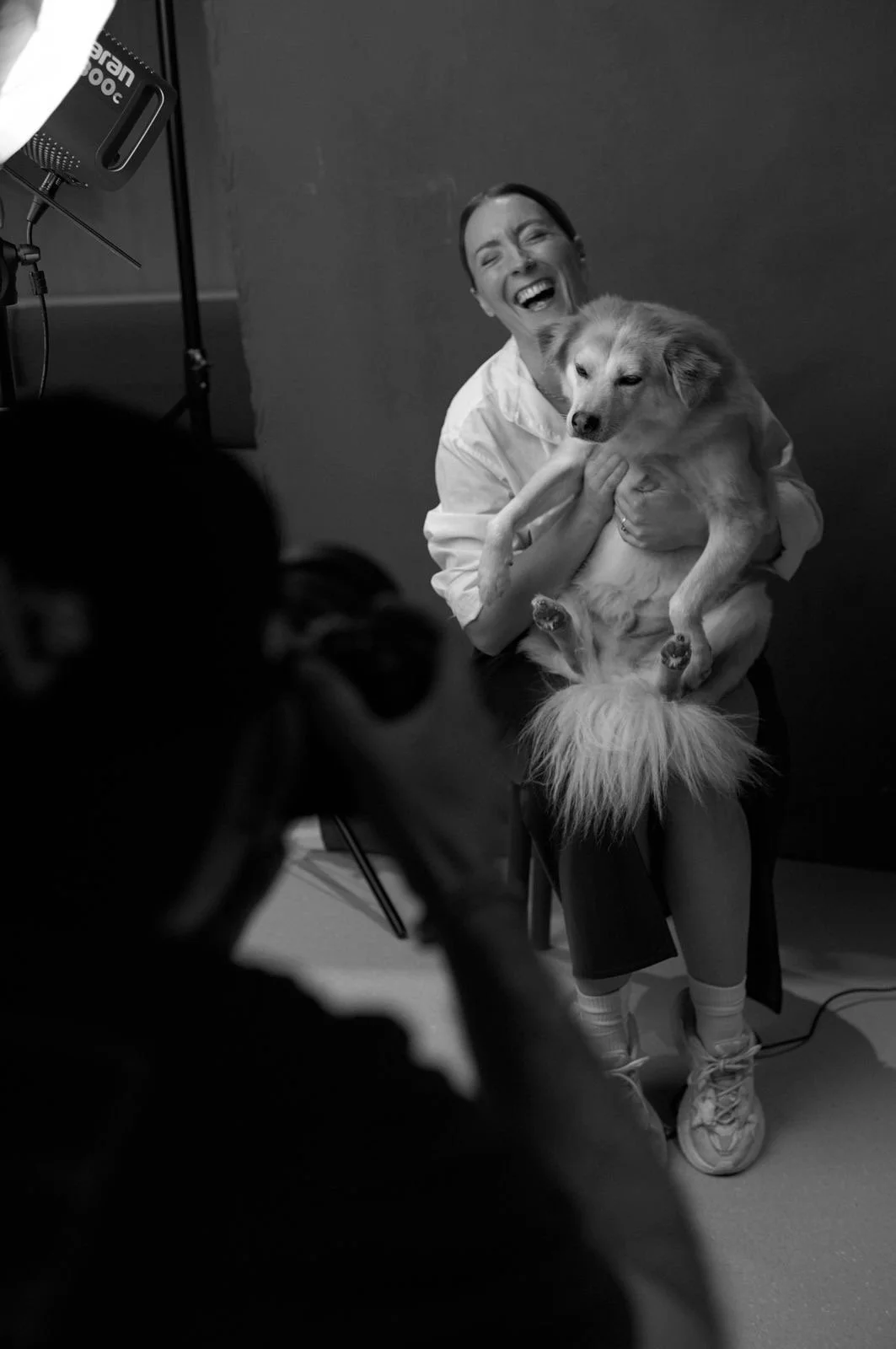 Blick hinter die Kulissen eines Portraitshootings: Eine lachende Person mit Hund vor der Kamera, in Schwarz-Weiß.