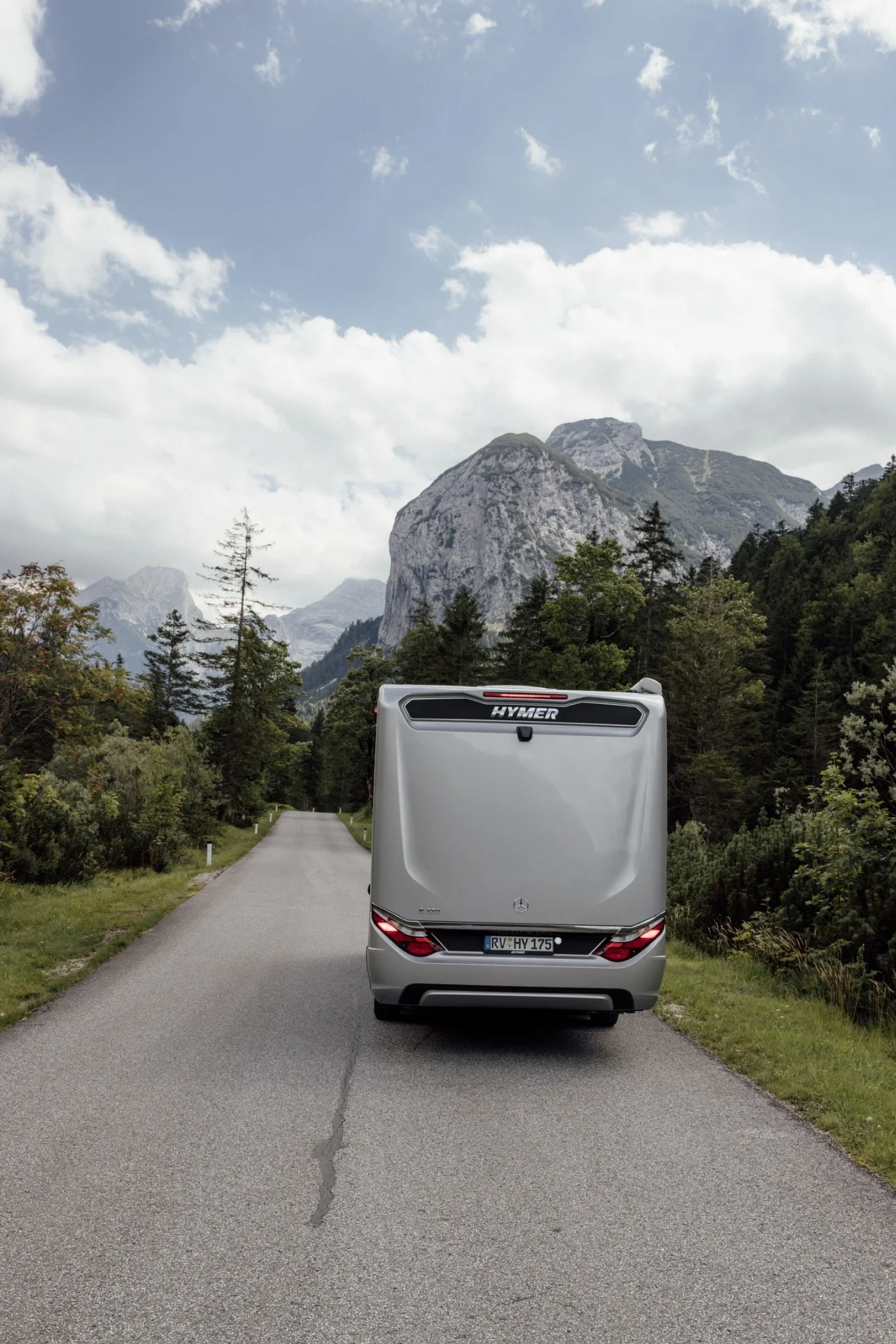 Hymer-Wohnmobil auf einer schmalen Straße vor bewaldeten Bergen.