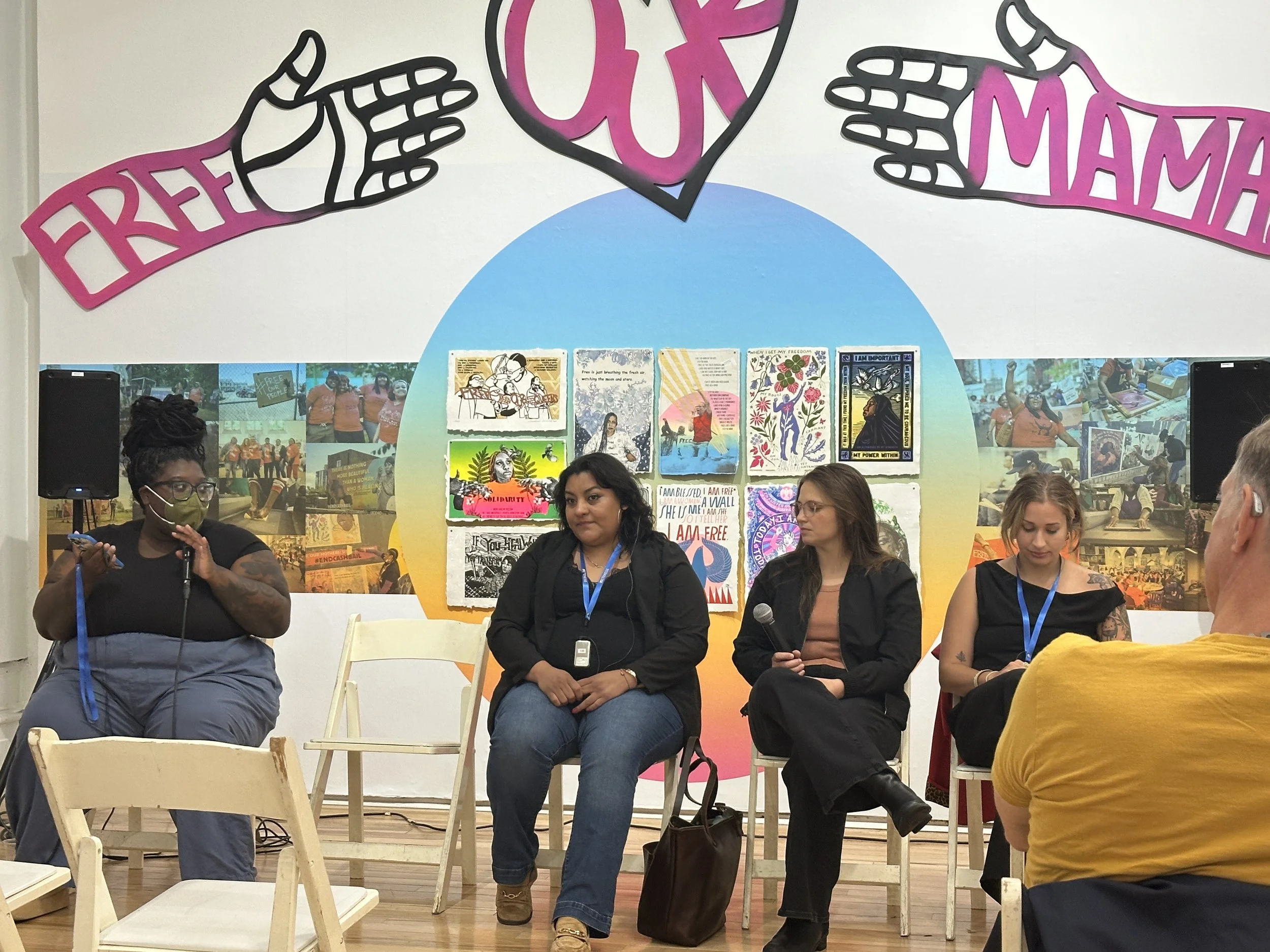 Panel discussion about the criminalization of immigrants with images from the Let's Get Free Exhibit in the background including a sign that says Free Our Mamas.