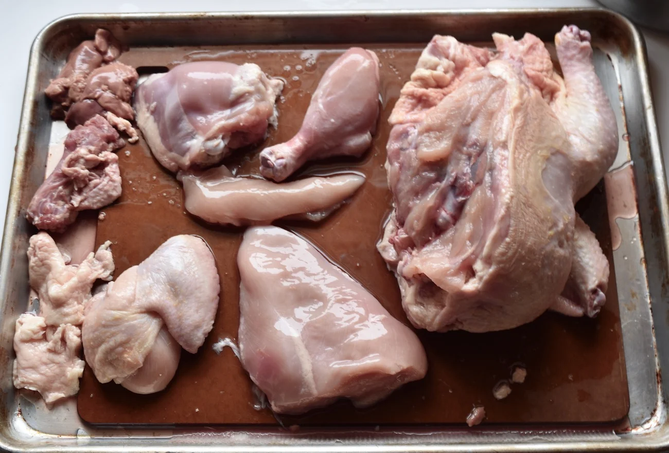 Clockwise from drumstick: skinned drumstick, chicken breast tender, skinned chicken breast, wing with breast meat, chicken skin, chicken neck and gizzard, chicken liver. When cutting up chicken I put my board inside a half sheet pan to contain the mess.