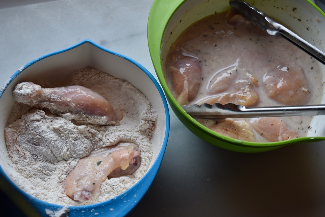 Pick up the soaking chicken pieces with tongs, let them drain, and put them in the flour mixture. Toss them around to coat on all sides. 
