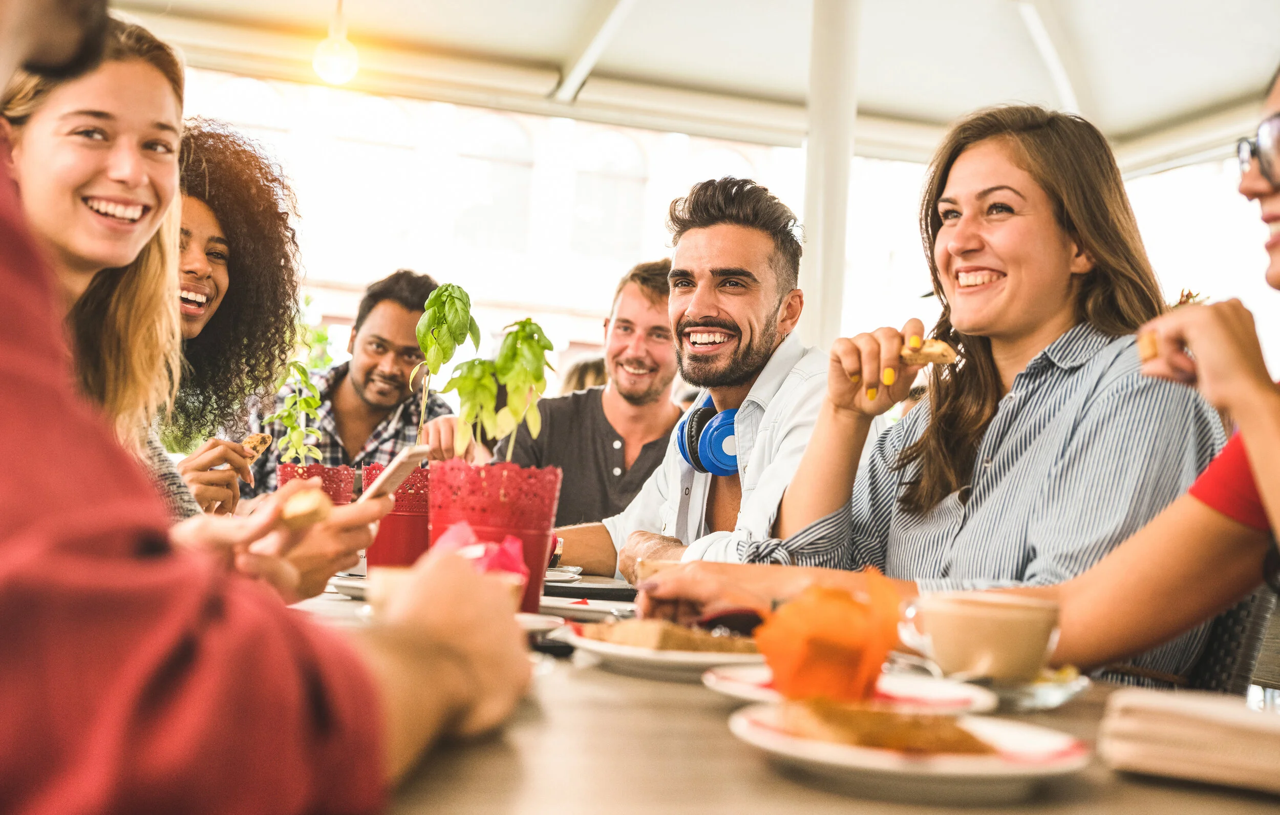 A diverse group of friends enjoying a meal together at a restaurant or cafe, smiling and talking.