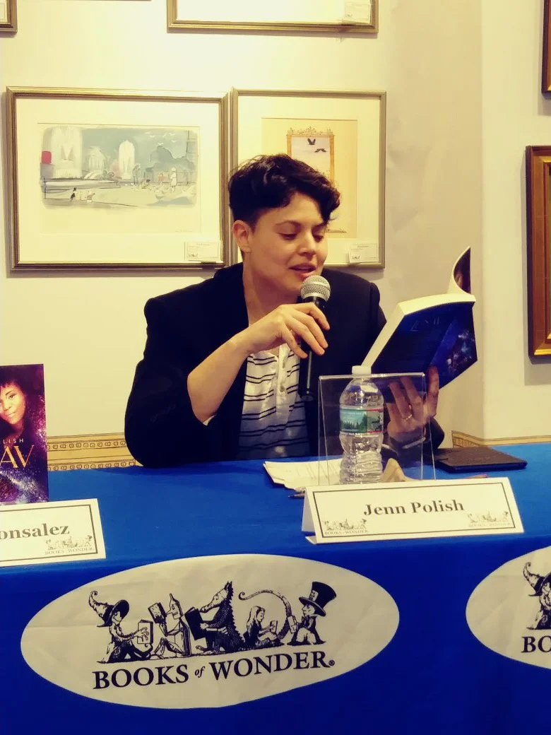 Jenn Polish, center, seated at a table at their book launch event at Books of Wonder, reading from their debut novel, LUNAV. Photo by the wonderful Gabby Abbate.